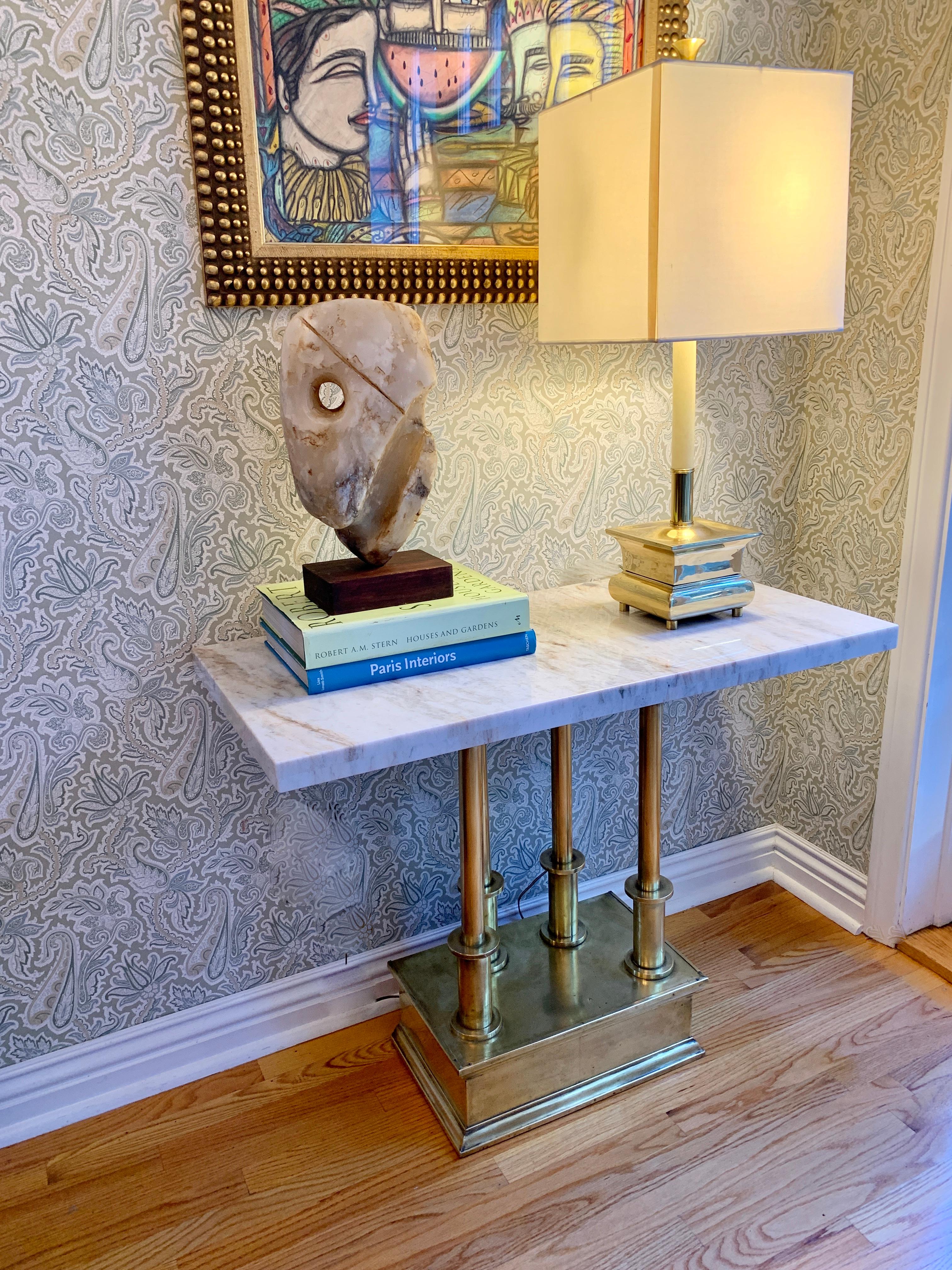 A brass console base of four architectural columns with periodic spheres - the top is honed white marble. 

The vintage piece has been partially polished giving the piece a bit of brilliant sheen. The brass wraps around the front - the rear is not