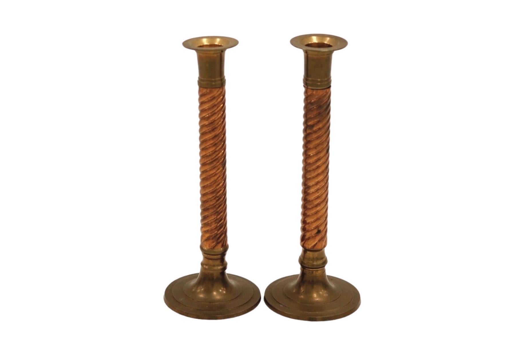 A pair of barley twist brass and copper candlestick holders. Solid brass is decorated with twisted reeded copper columns. Broad rimmed capitals mirror round elegant bases. Dimensions per candlestick.
