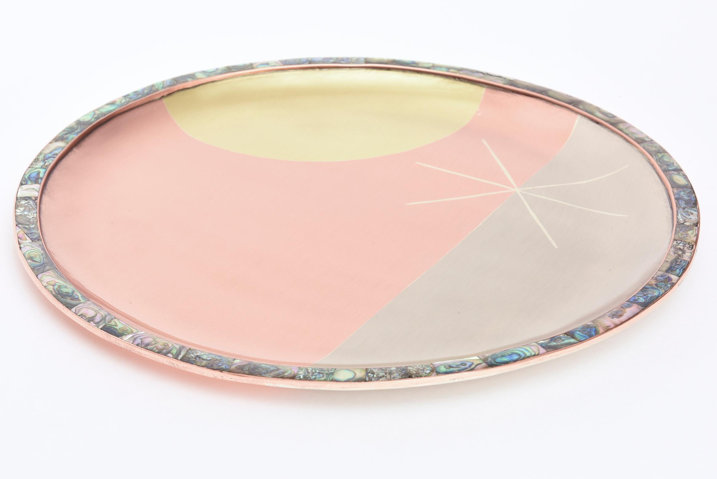 This lovely Mid-Century Modern mixed metal signed round tray is a combination of brushed brass, copper, silver and sterling silver as the star surrounded by a mosaic of beautiful abalone as the perimeter. It is hallmarked on the back E. Cabella C.A.