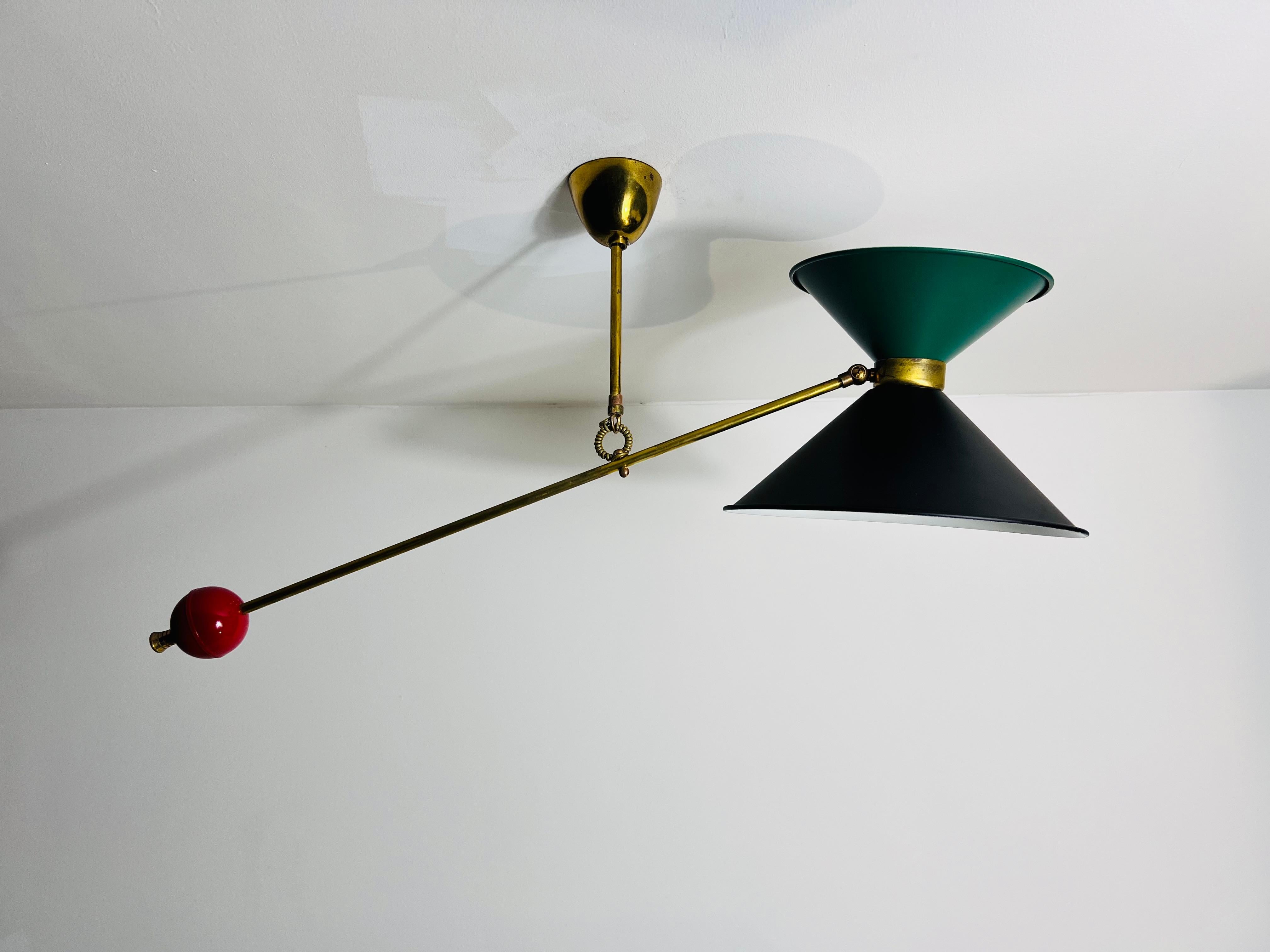 Questa eccezionale lampada a sospensione attribuita al famoso designer francese Pierre Guariche, risalente agli anni '50, è un vero capolavoro del design moderno di metà secolo. Realizzata in ottone, la lampada presenta un sorprendente contrappeso