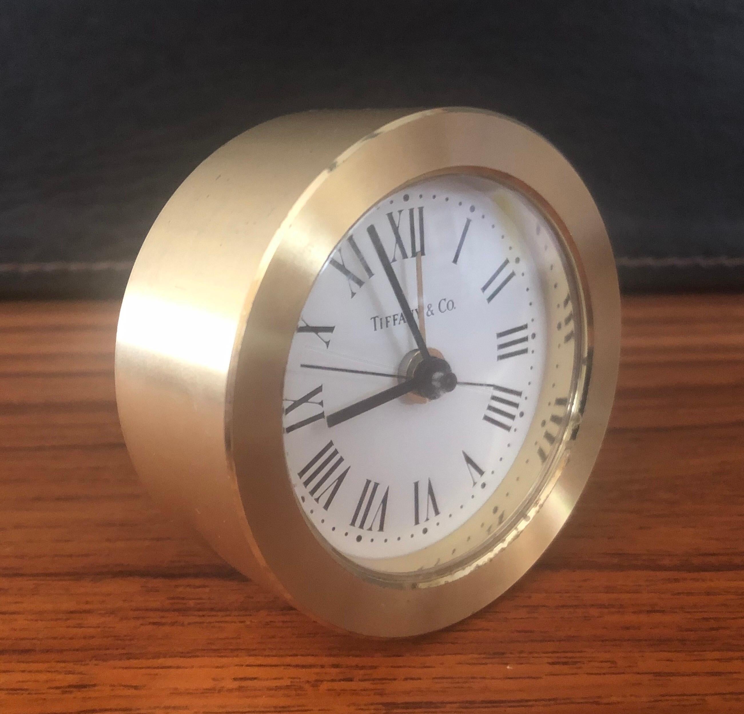 A very nice round brass desk alarm clock by Tiffany & Co., circa 1980s. The clock has a quartz movement and is made in Germany; the case is made of brushed brass and has formed Roman numeral for hour markers. The piece features a white dial with