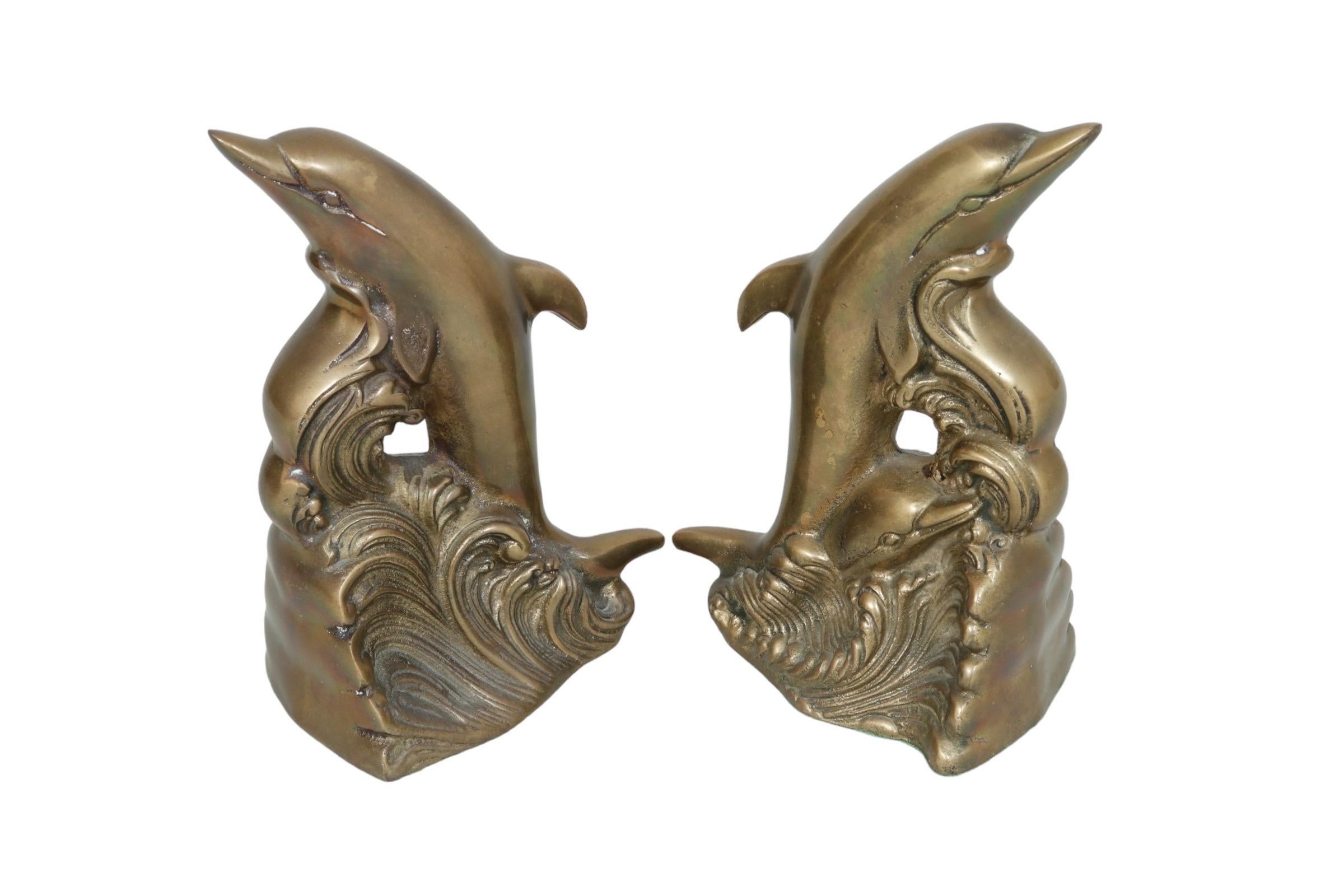A pair of brass bookends made by Andrea by Sadek. Each is cast in the shape of a dolphin with calf breaching a scrolling wave. Felted on the bottom, with the gold maker's label that reads “Andrea by Sadek, made in Korea”. Dimensions per bookend.