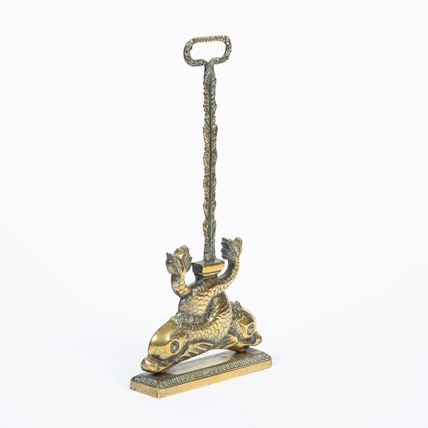 A brass door stop or door porter in the form of two intertwined dolphins, with a loop handle and iron weighted base.

Weight: 2.75 kg - 6 1/4 lbs
