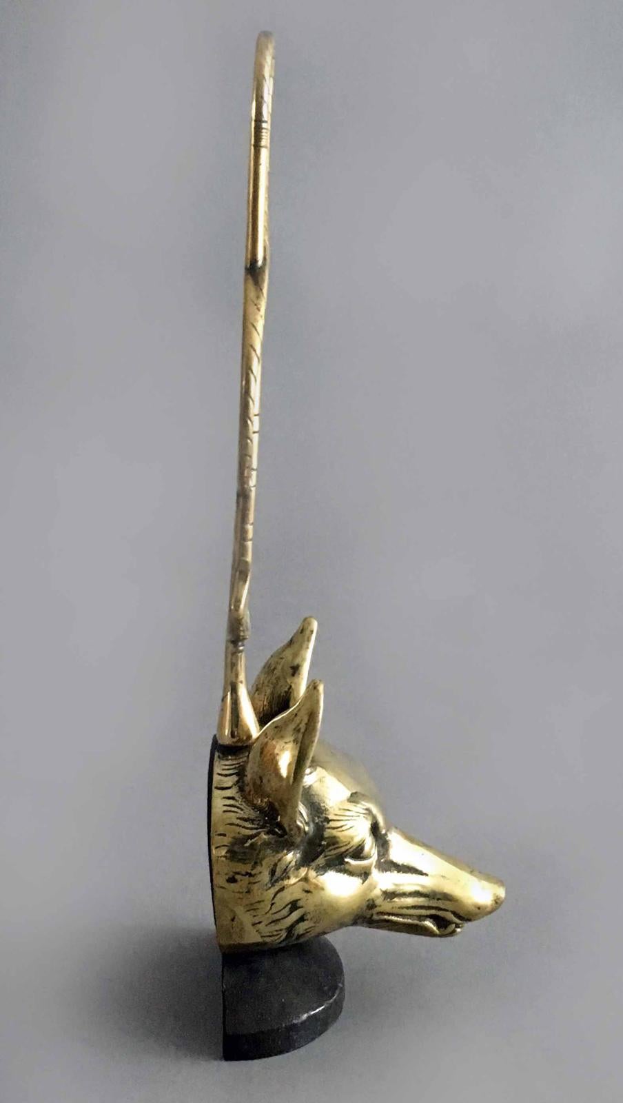 A brass doorstop in the form of a fox’s head with the handle in the form of a riding crop. The doorstop is weighted with lead.