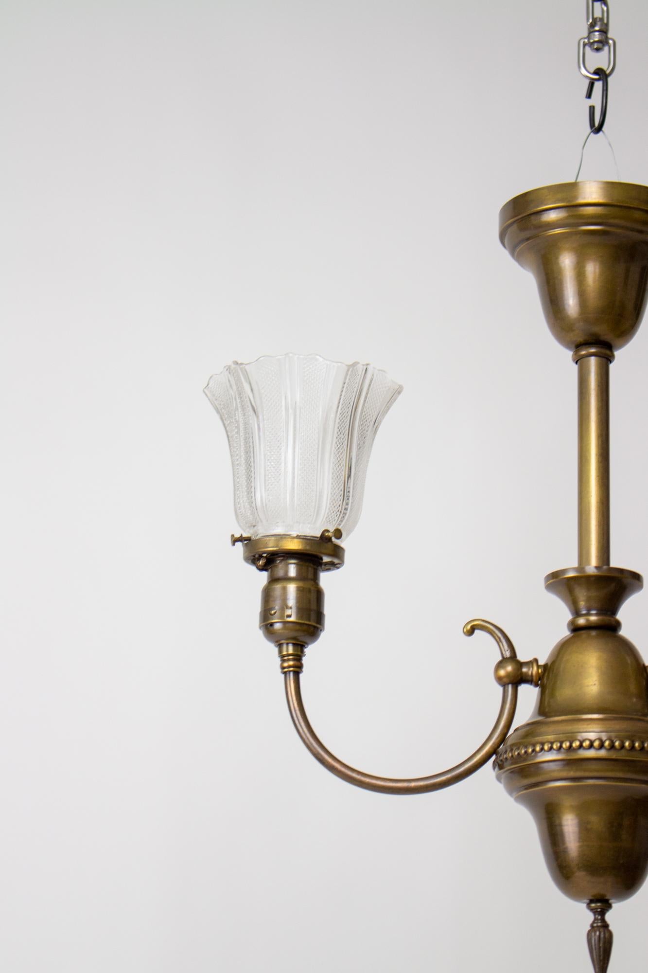 Brass early electric fixture with Prismatic glass shades. Two lights, Victorian style with a slip canopy and two arms curving up from a central acorn shaped stem piece. Finished on the bottom with a cast brass ornamental finial. Glass is original,