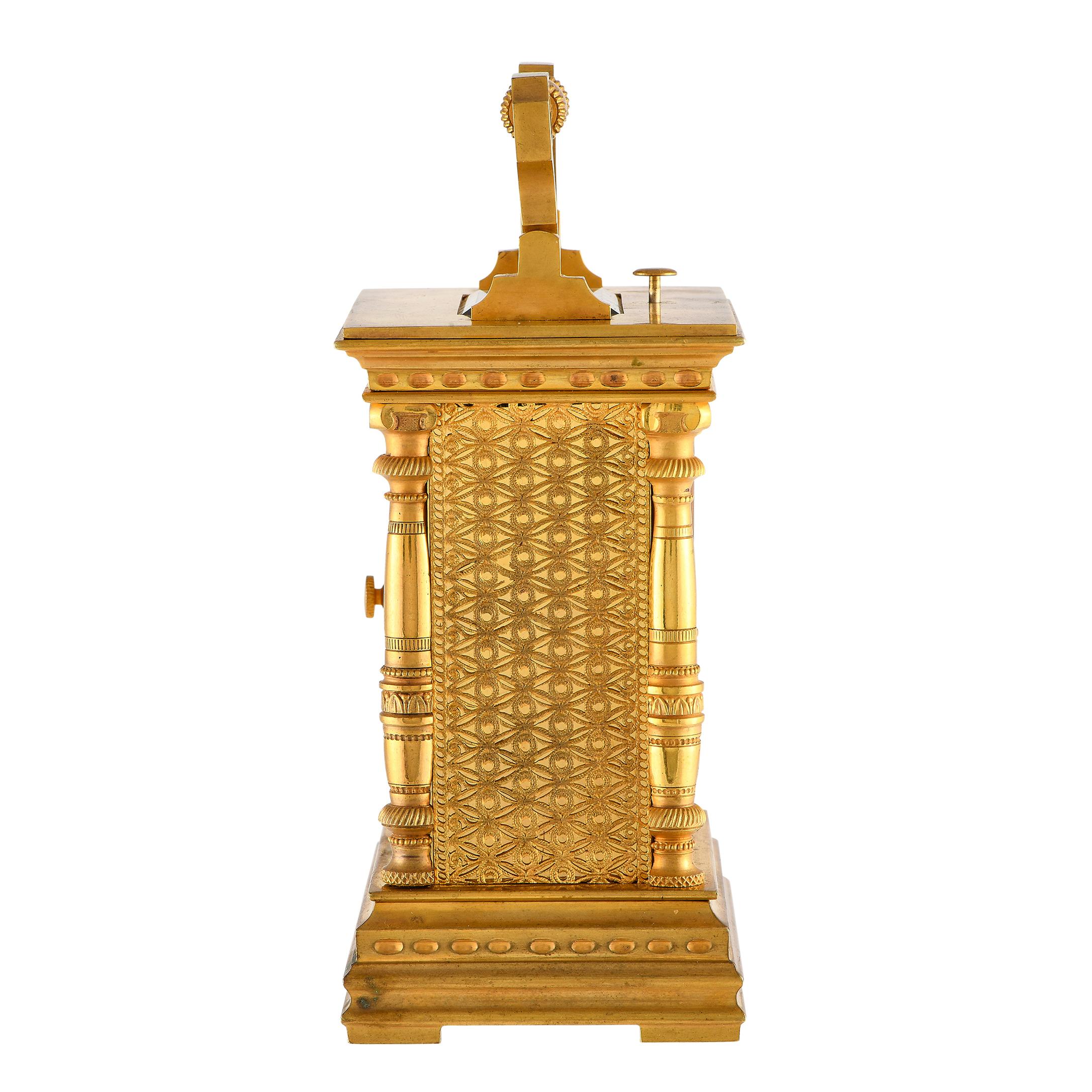Intricately crafted in gilt brass, here is a fine French carriage clock from the late 19th to early 20th century. This analog timekeeper of a discernible style features heavily decorated columns, ornately patterned sides and back, and an enamel dial