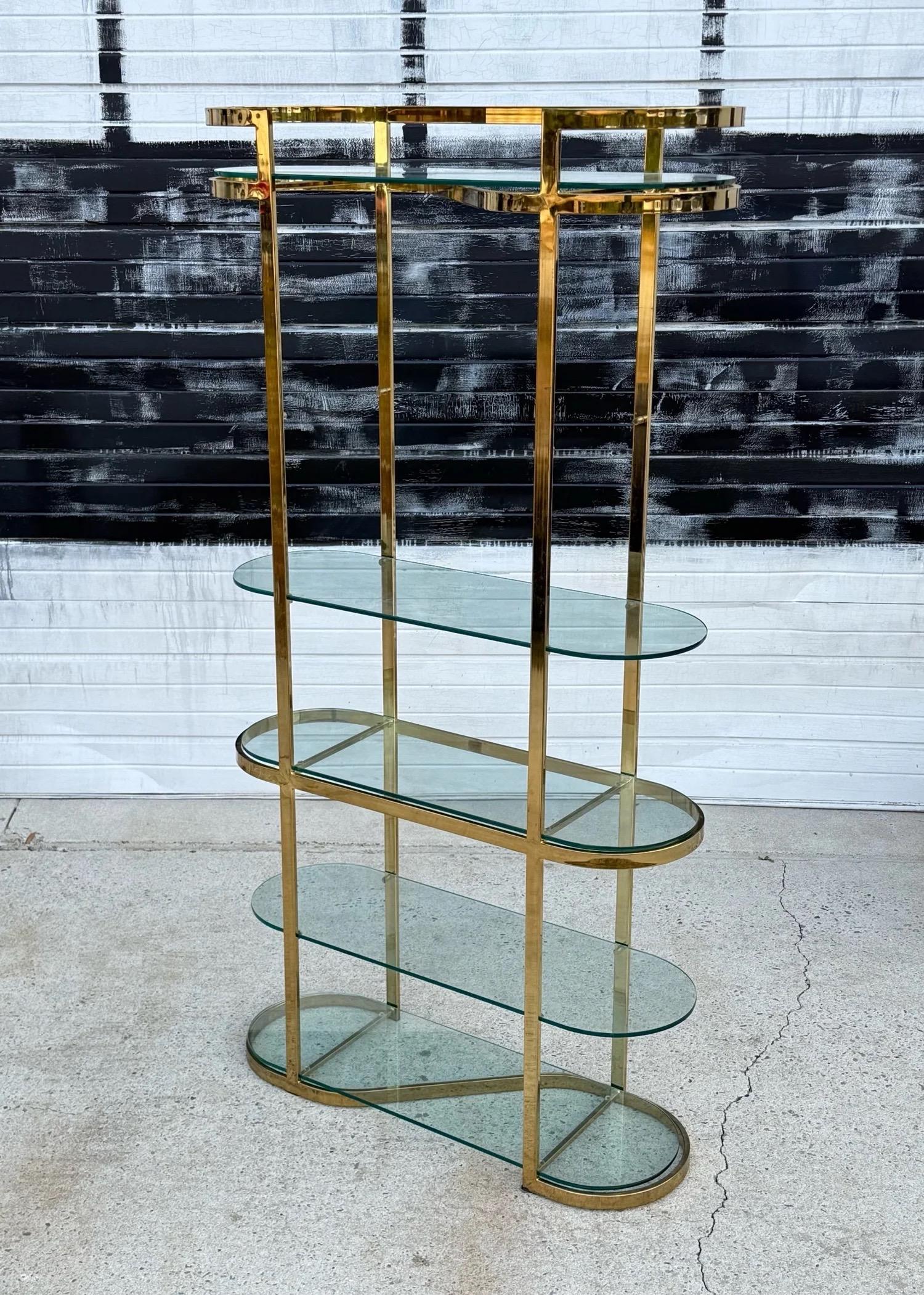 Etagère en laiton et verre dans le style de Milo Baughman. Cette pièce est haute, mais aussi très mince, ce qui permet une présentation parfaite sans sacrifier trop d'espace au sol. Cinq inserts en verre de forme ovale permettent de créer des