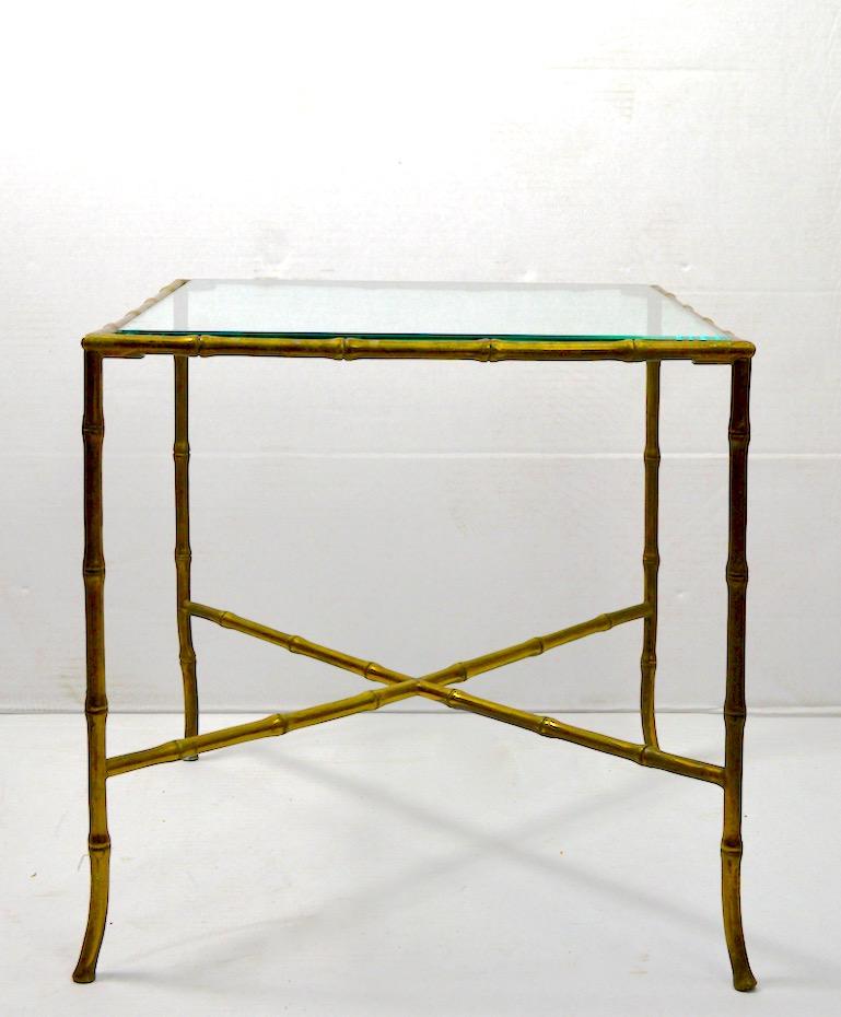 Stylish faux bamboo side table in cast brass, made in Italy, after Maison Jansen. This example is in very good original condition, with original beveled plate glass top. The finish shows expected patina, as pictured. Fine quality construction, clean