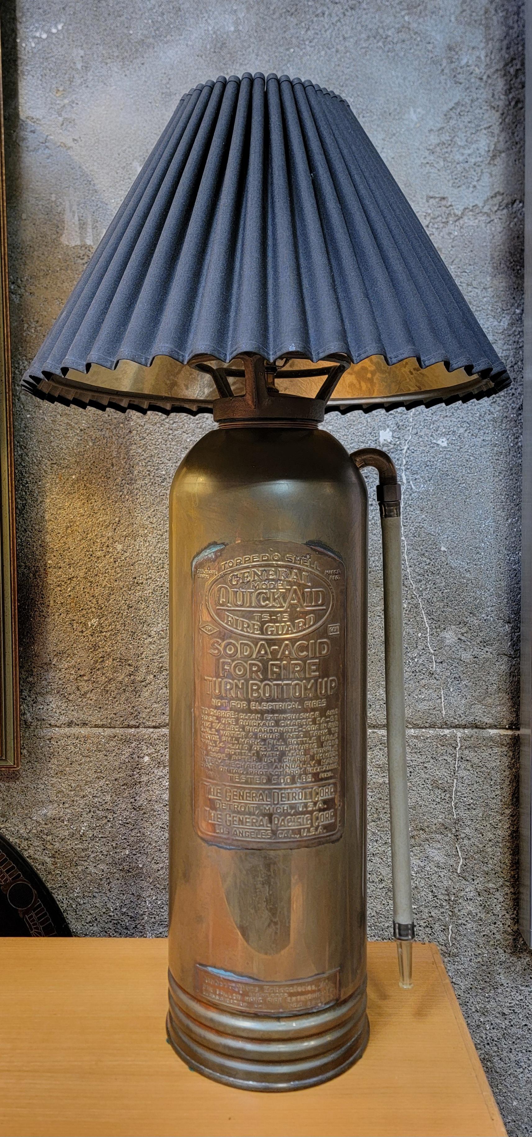 An antique brass fire extinguisher repurposed into a table lamp. Fluted shade included. Electrical socket in working order. Made by The General Pacific Corporation, Los Angeles, California. 