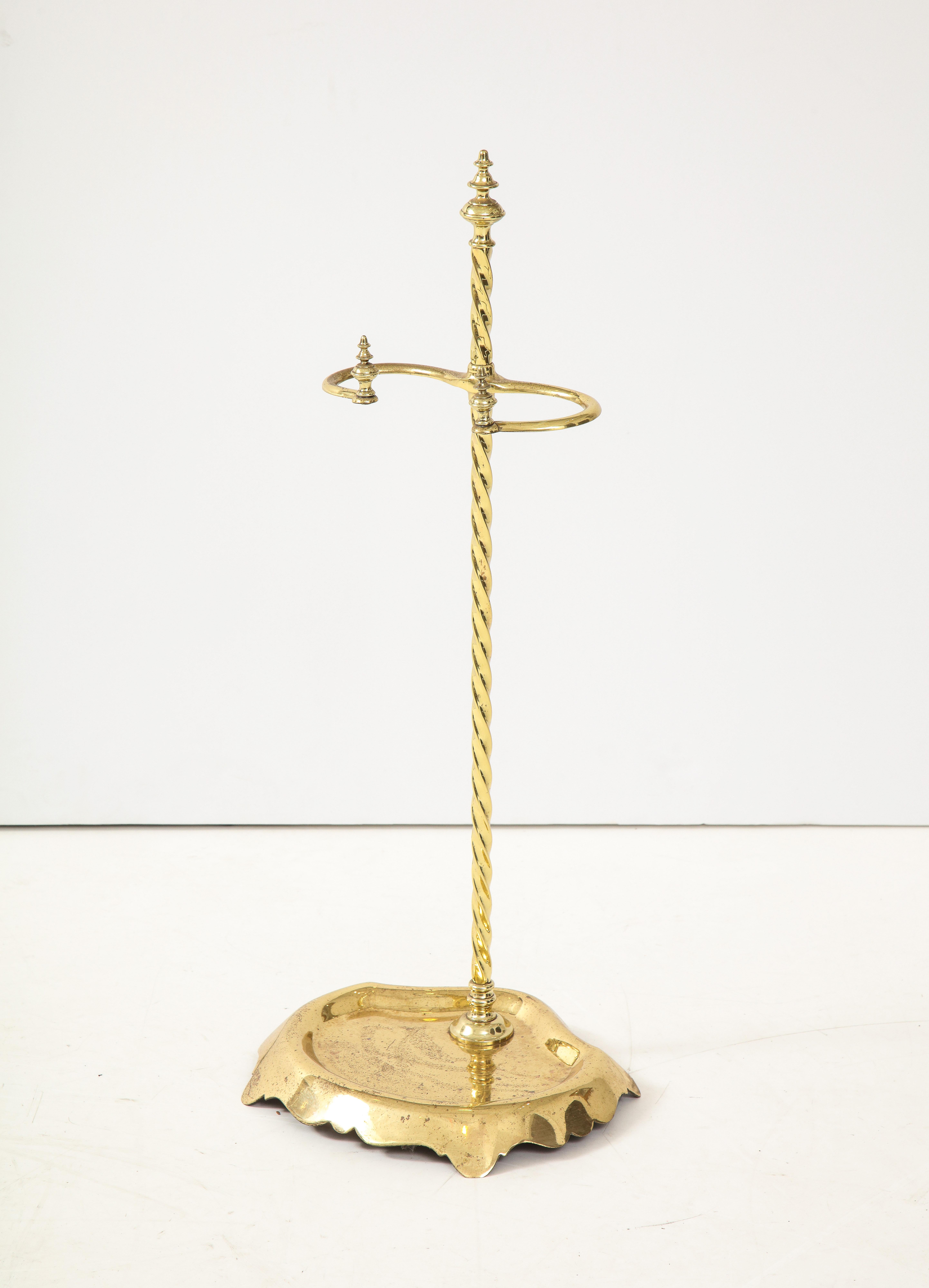 Good 19th century brass fire tool stand having turned steeple finial over spiral twist shaft with two crook arms over cast brass base with scalloped shape and feet.
 