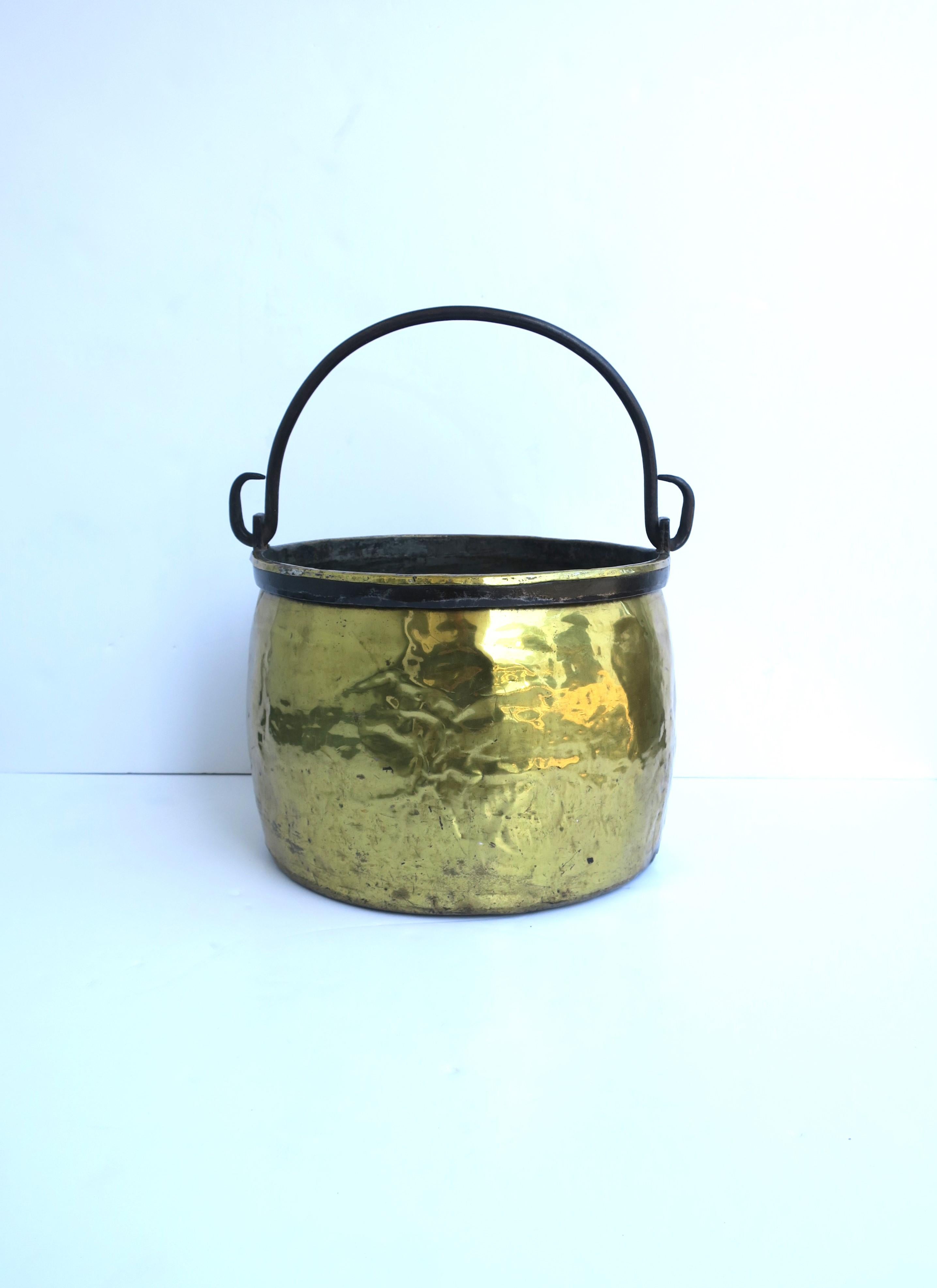 A relatively large Dutch brass fireplace bucket or pot with blacked iron handle, circa 19th century, Holland. Piece is round, brass, with a blackened iron band around top and handle to match, perfect for carrying/holding firewood (as demonstrated),