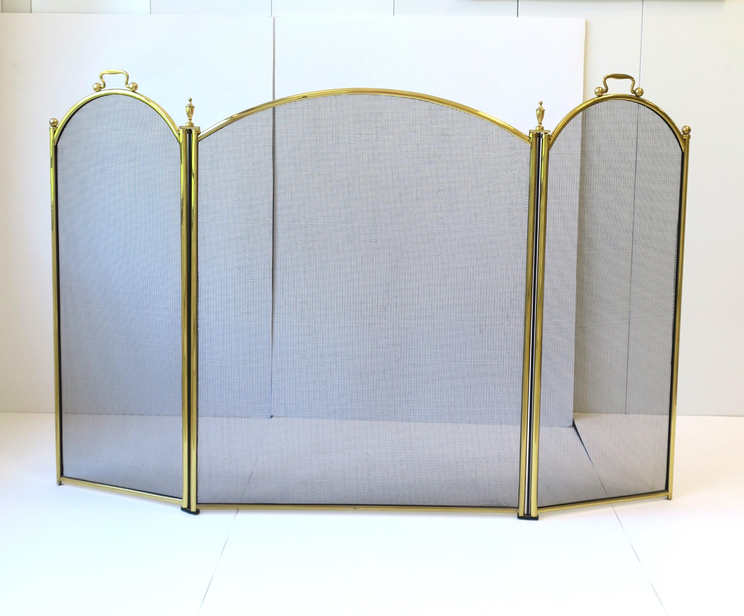 A brass frame fireplace screen with handles and finial details, circa late-20th century. Screen is a trifold with brass frame, black mesh metal screen, brass handles and finials. The trifold is nice because it allows no obstruction to front of