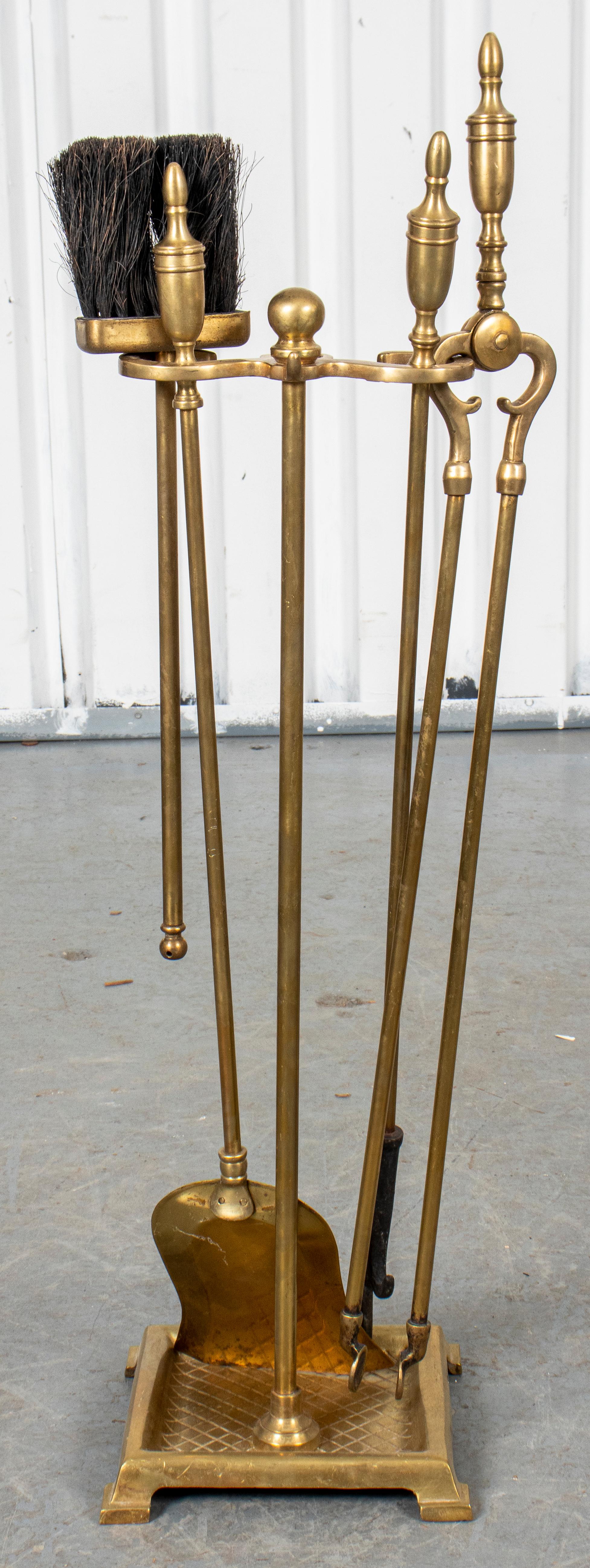 Brass fireplace tool set comprising a stand, tongs, shovel, brush, and log poker, with slim urn finial motif. Measures: 30” H x 10” W x 10” D.