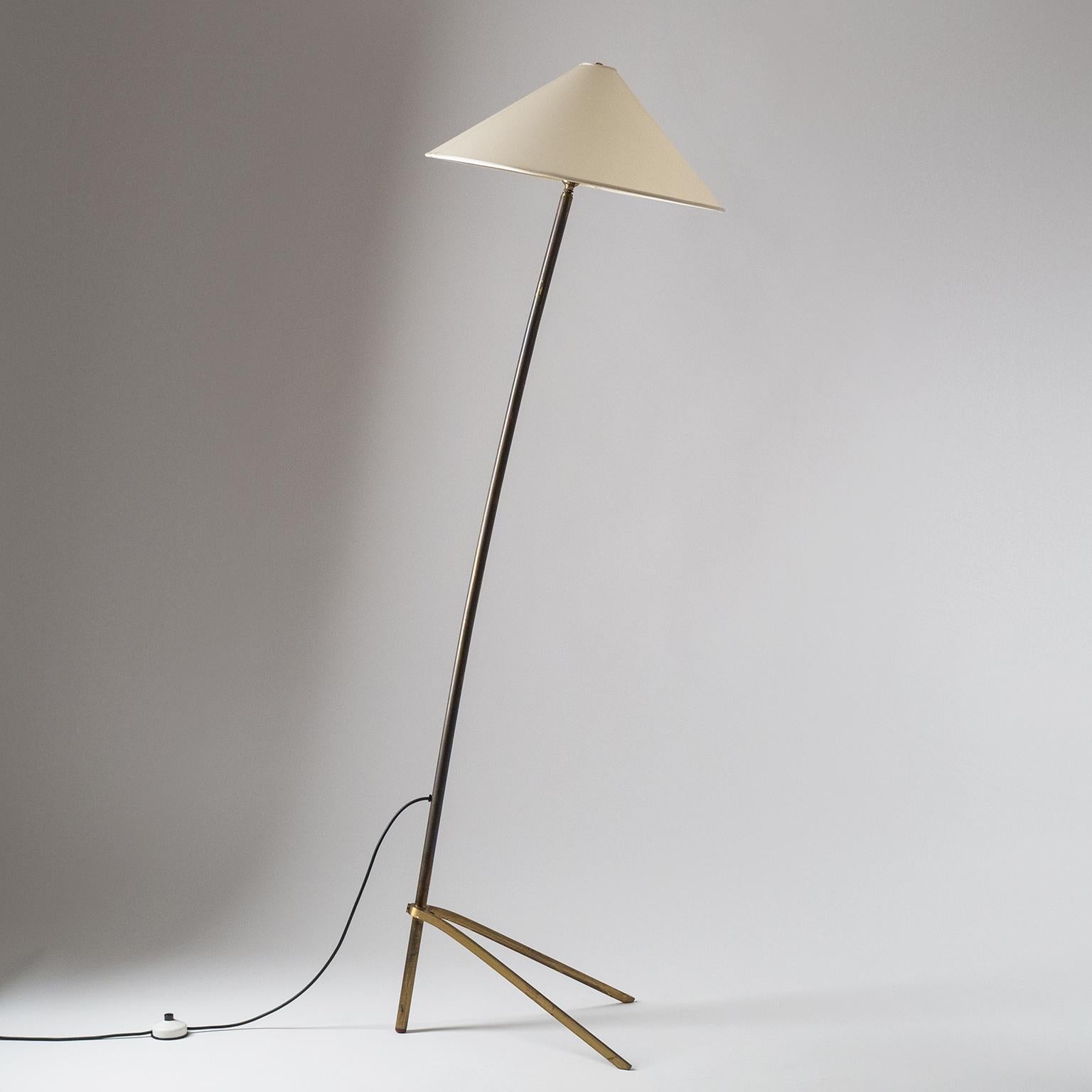Minimalist brass floor lamp, circa 1950. Elegant arching brass stem with tripod base. The original shade has new parchment covering and can pivot for different lighting effects. One original brass E27 socket with new wiring.