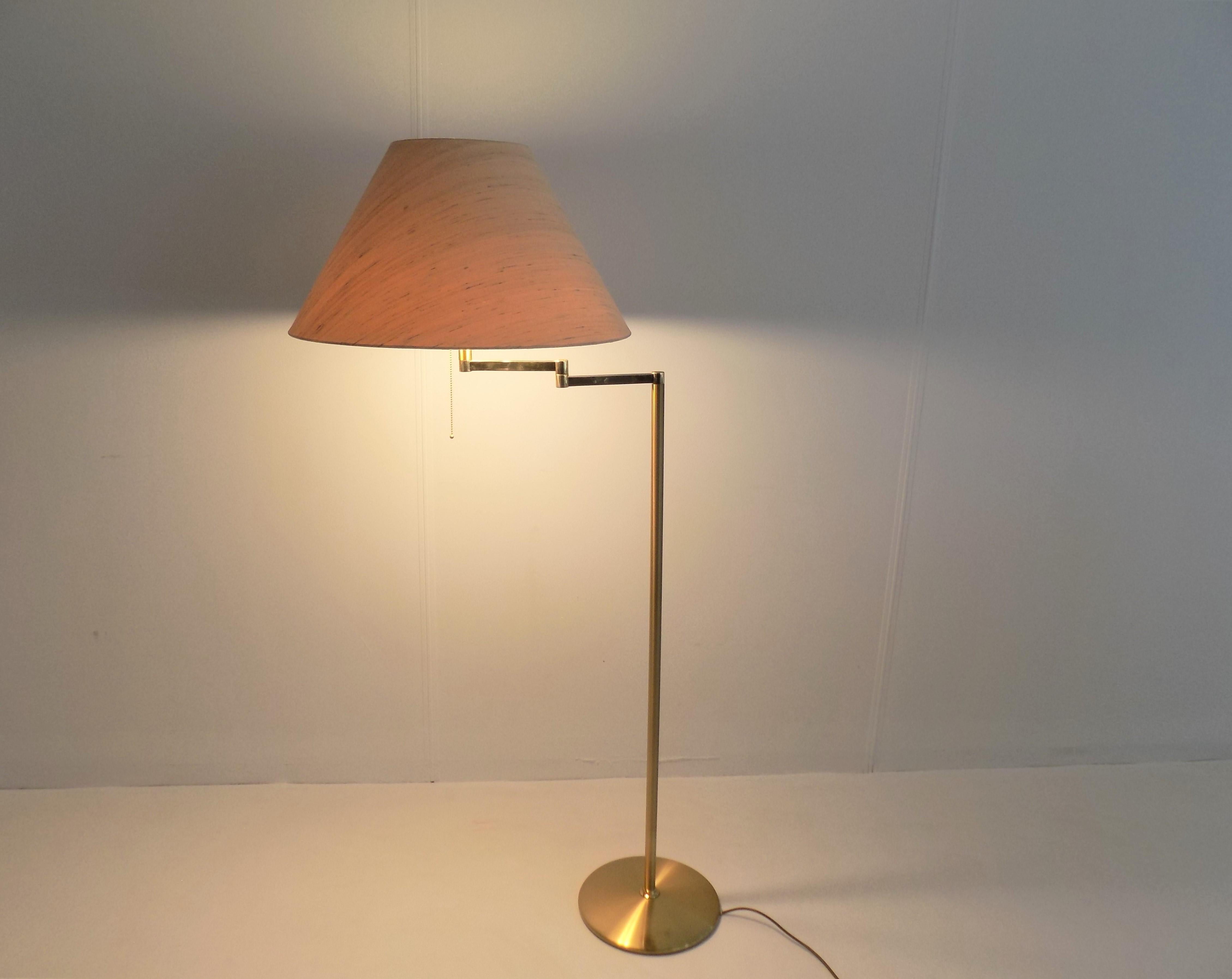 This large brass floor lamp is in good condition. The brass base shows slight signs of wear, the natural-colored lampshade with a mottled linen structure is impeccable. The lamp can be used variably via the swivel arm and has 3 light points in the