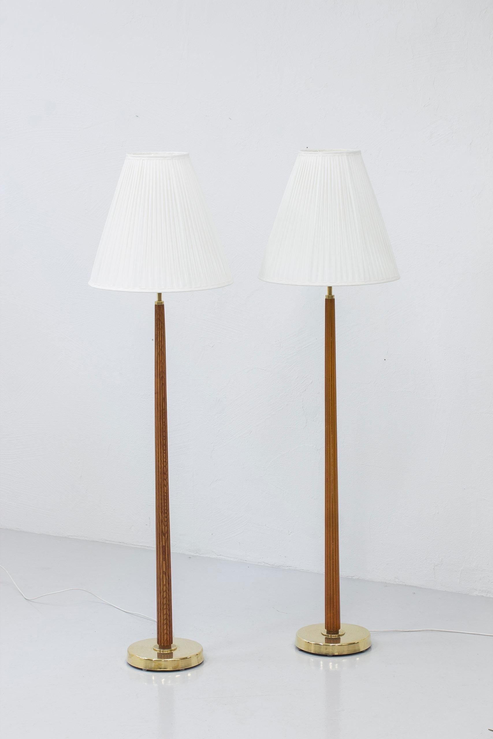 Floor lamps model 522 designed by Hans Bergström. Produced by Ateljé Lyktan during the 1940-50s. Made from brass with wooden stems of solid elm. Opaline glass shades with a hand sewn pleated lamp shade resting on the glass. The lamps have two light