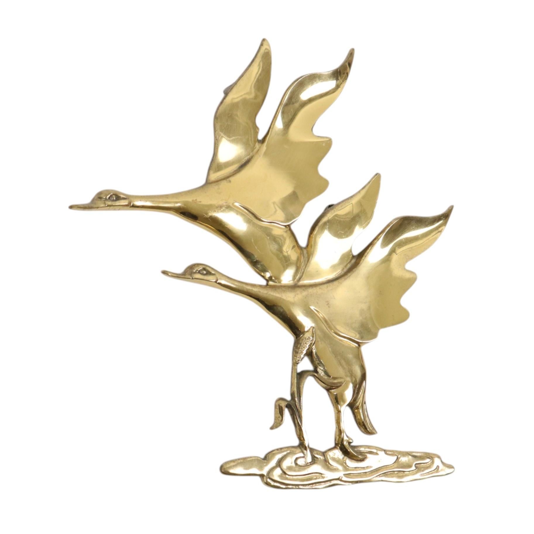 Elegant mid century wall decoration, image of a pair of geese flying up from a waterhole, stylishly styled and made of high quality brass, authentic vintage object from around the 60s.

Hollywood Regency style with a touch of art deco, this