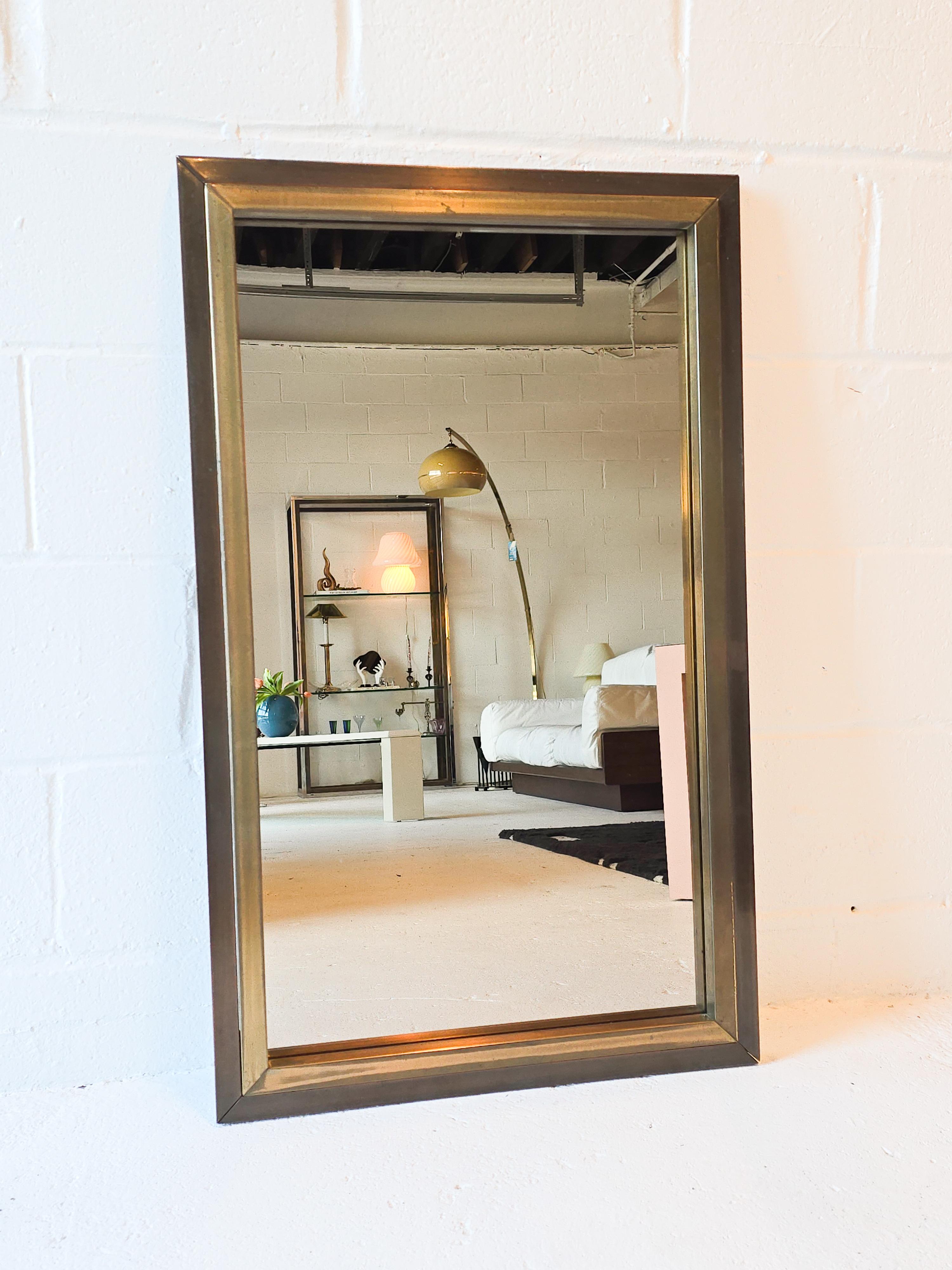Magnifique miroir mural en verre teinté avec cadre en laiton. Le cadre est double, avec des métaux en laiton patiné plus clairs et plus foncés. Le miroir teinté est d'une teinte rosée semblable au bronze. Le cadre en laiton présente une belle