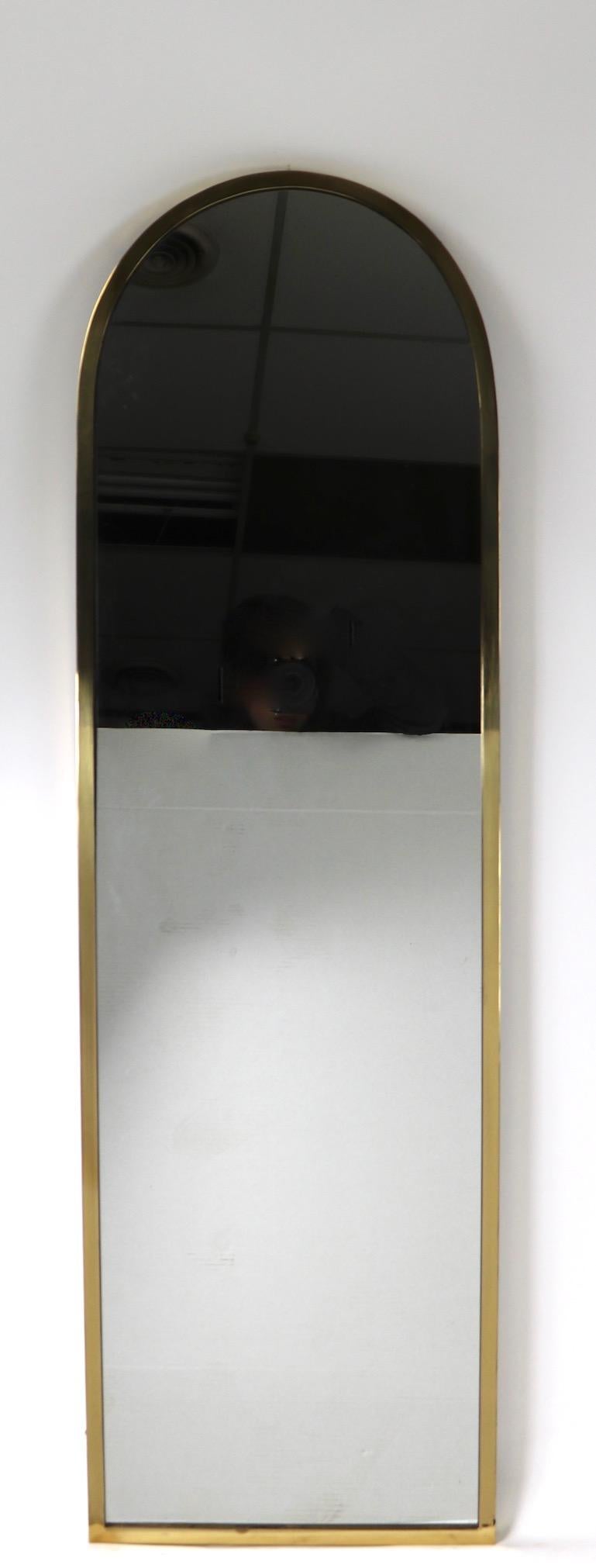 Brass frame of tombstone form, with plate glass mirror, labeled Made in Italy, attributed to Mastercrafters. Simple elegant design, high quality materials, and construction.
 Very good original condition, clean ready to hang.