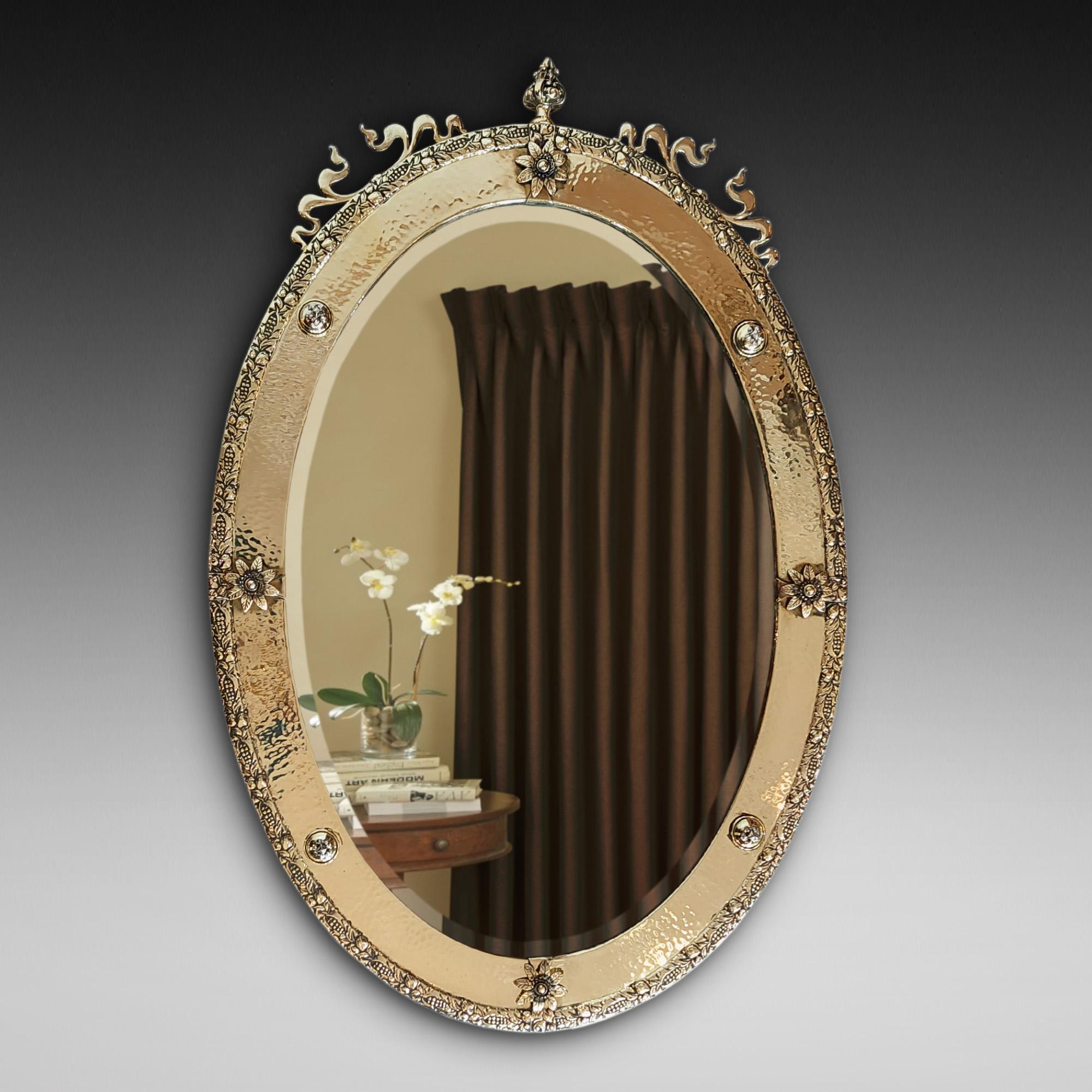 Brass Framed Arts and Crafts Mirror with beaten brass rim decorated with finial, ribbons, rosettes and bobbins 28
