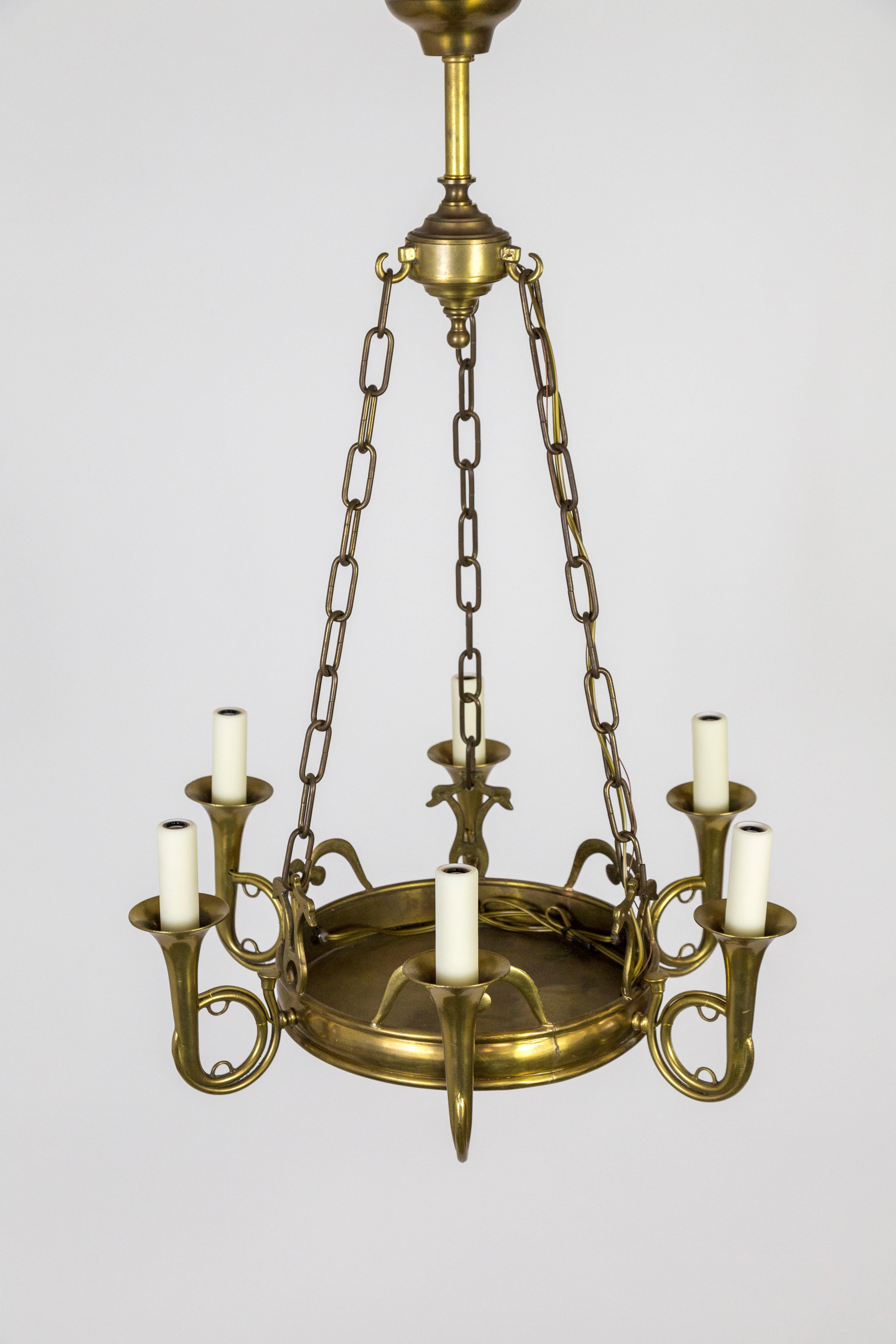 A solid brass chandelier in the form of 6 French horns pointing up with candle-style lights surrounding a large, flat dish. A streamlined, well-crafted design with 3 chains to center finial top finial, with a short stem to the canopy. Early 20th