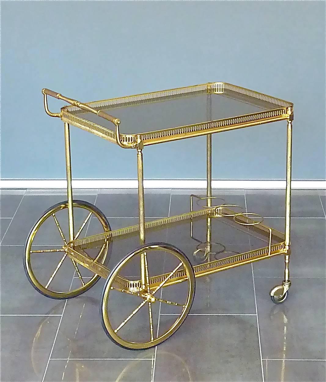 Amazing vintage bar cart, drinks or serving table or trolley made by Maison Baguès Paris, France, circa 1950. It is made of partly patinated brass, brass metal and brown tinted glass. It has two detachable glass trays with a beautiful break-through