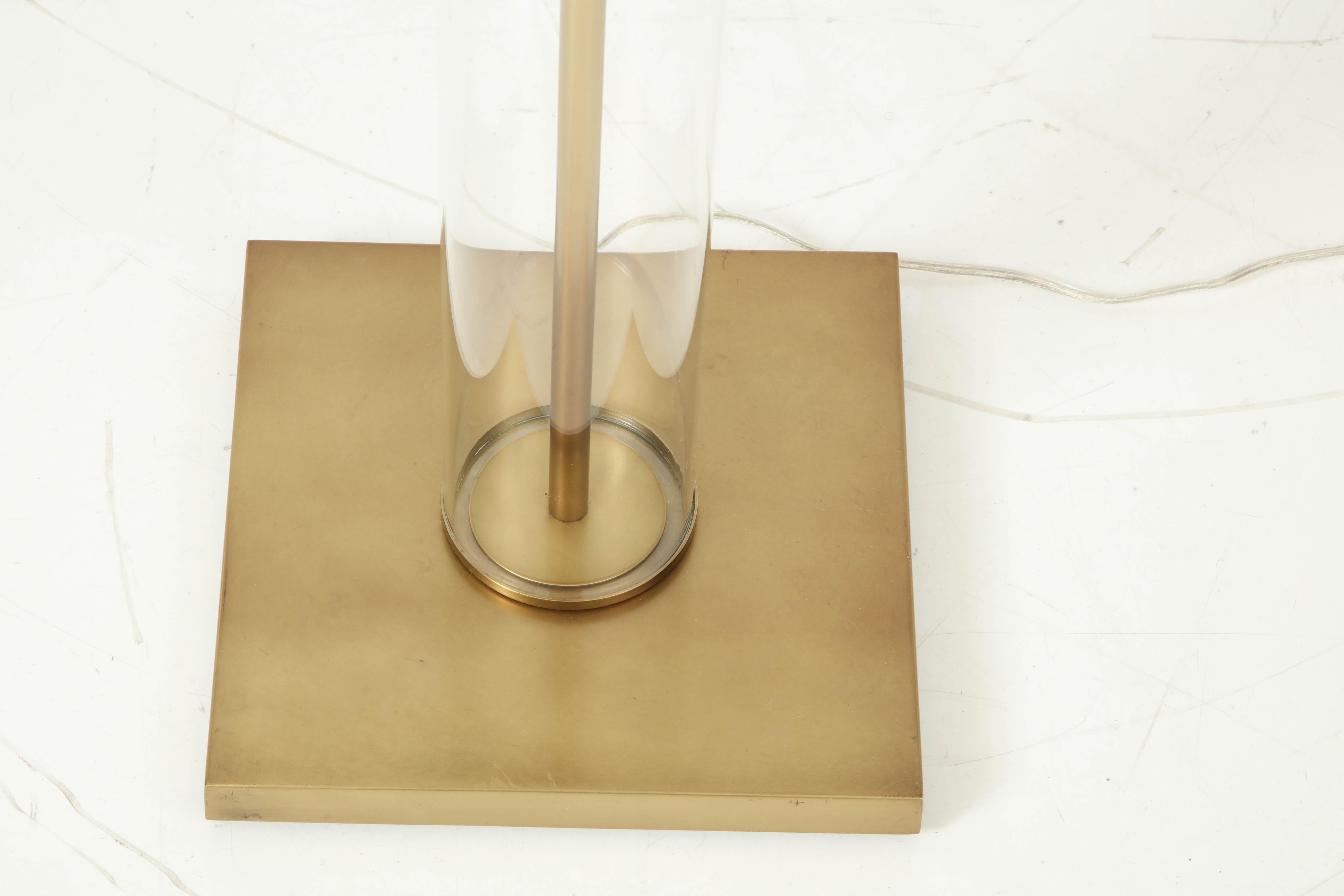 Sleek modernist floor lamp featuring a hollow glass tube resting on an aged brass base and with double pull chain sockets. Rewired for use in USA.