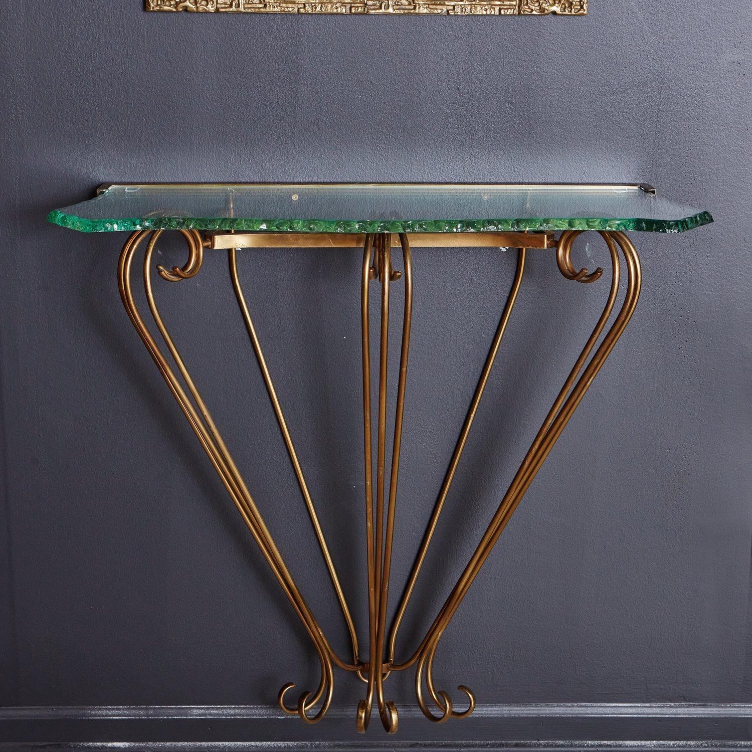 A stunning console table in the style of Fontana Arte. This console features a wall mounted patinated brass base with curled tubular details. It has a uniquely shaped glass top with raw, textured edges. Sourced in France, 20th Century.

