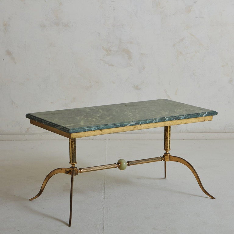 A 1940s French coffee table featuring a stunning rectangular green marble top with painterly veining and a beveled edge. This elegant table has a patinated brass base with four curved legs and a horizontal fluted stretcher with an onyx ball detail.