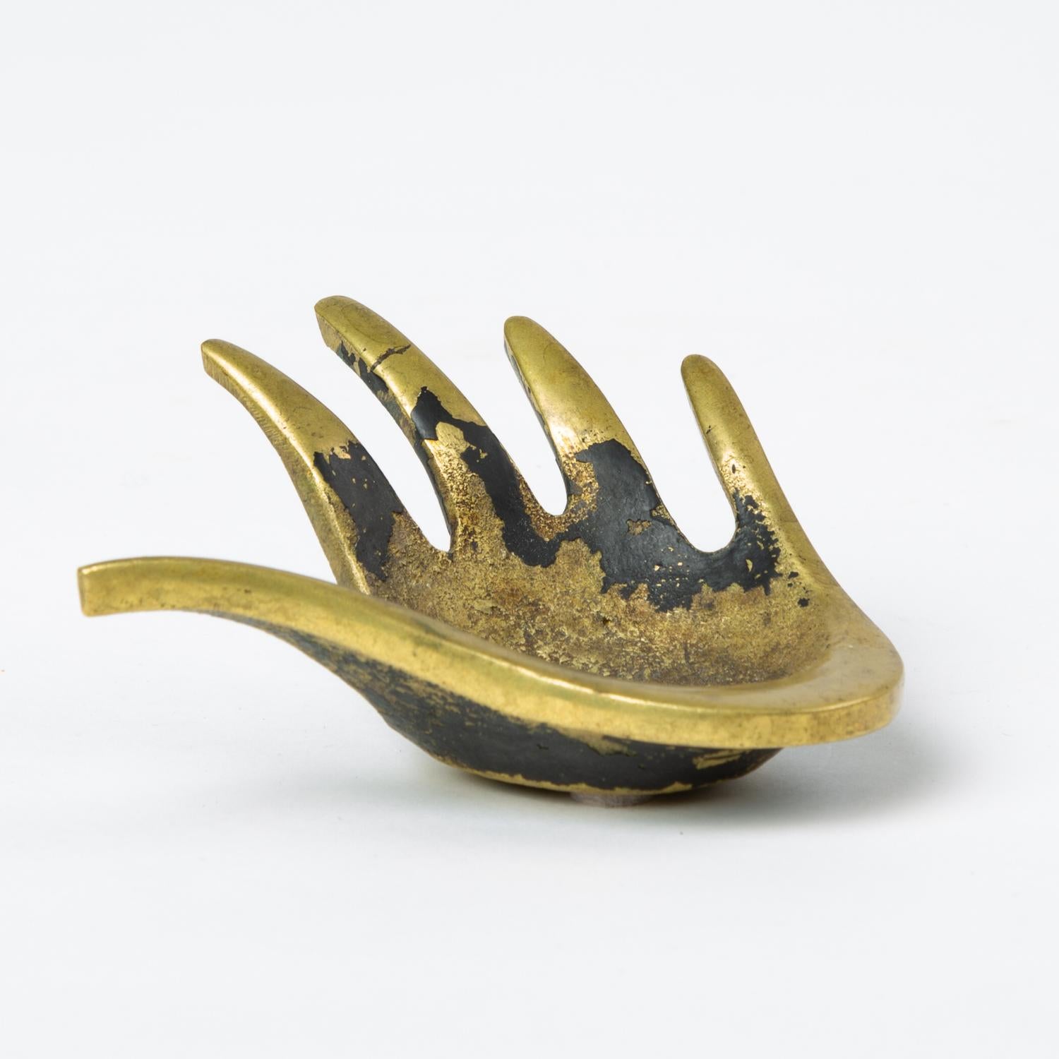 A multifunctional small brass bowl in the shape of an open hand lying palm up by Austrian ceramicist and metalworker Walter Bosse, produced in the 1950s through his partnership with Hertha Baller. The modernist object has pointed digits stretched