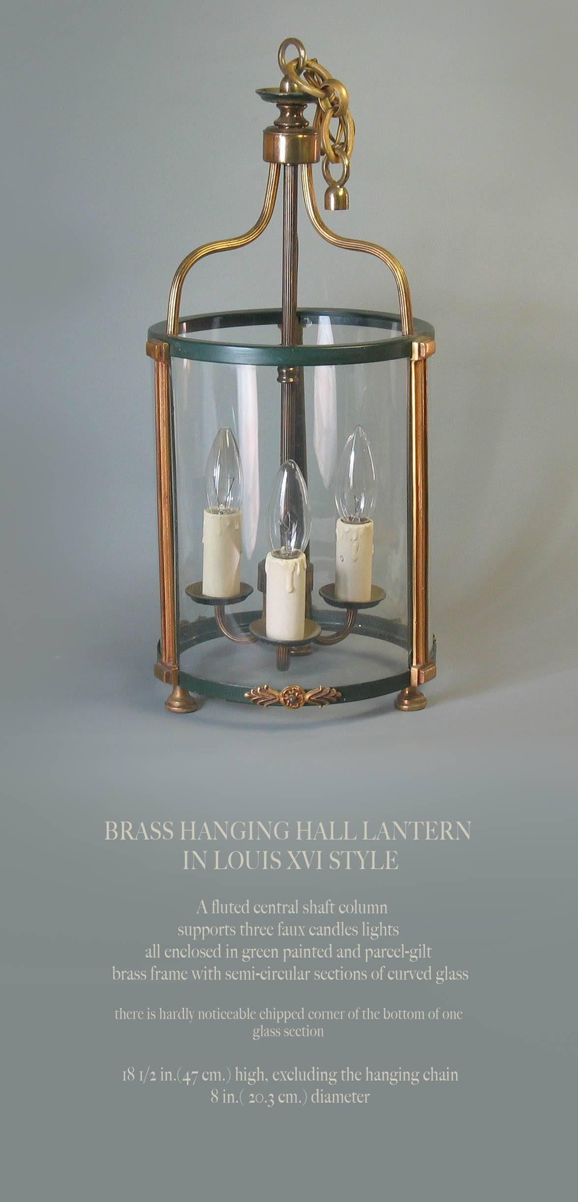 A brass hanging hall lantern in Louis XVI style, a fluted central shaft column supports three faux candle lights, all enclosed in green painted and parcel-gilt brass frame with semi-circular sections of curved glass. There is a hardly noticeable