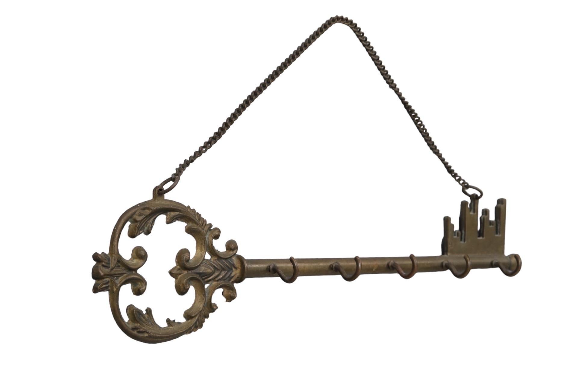 A large decorative brass key is cast with an acanthus scrolled bow and five small hooks on the stem. Hangs with a simple 12” chain.
  