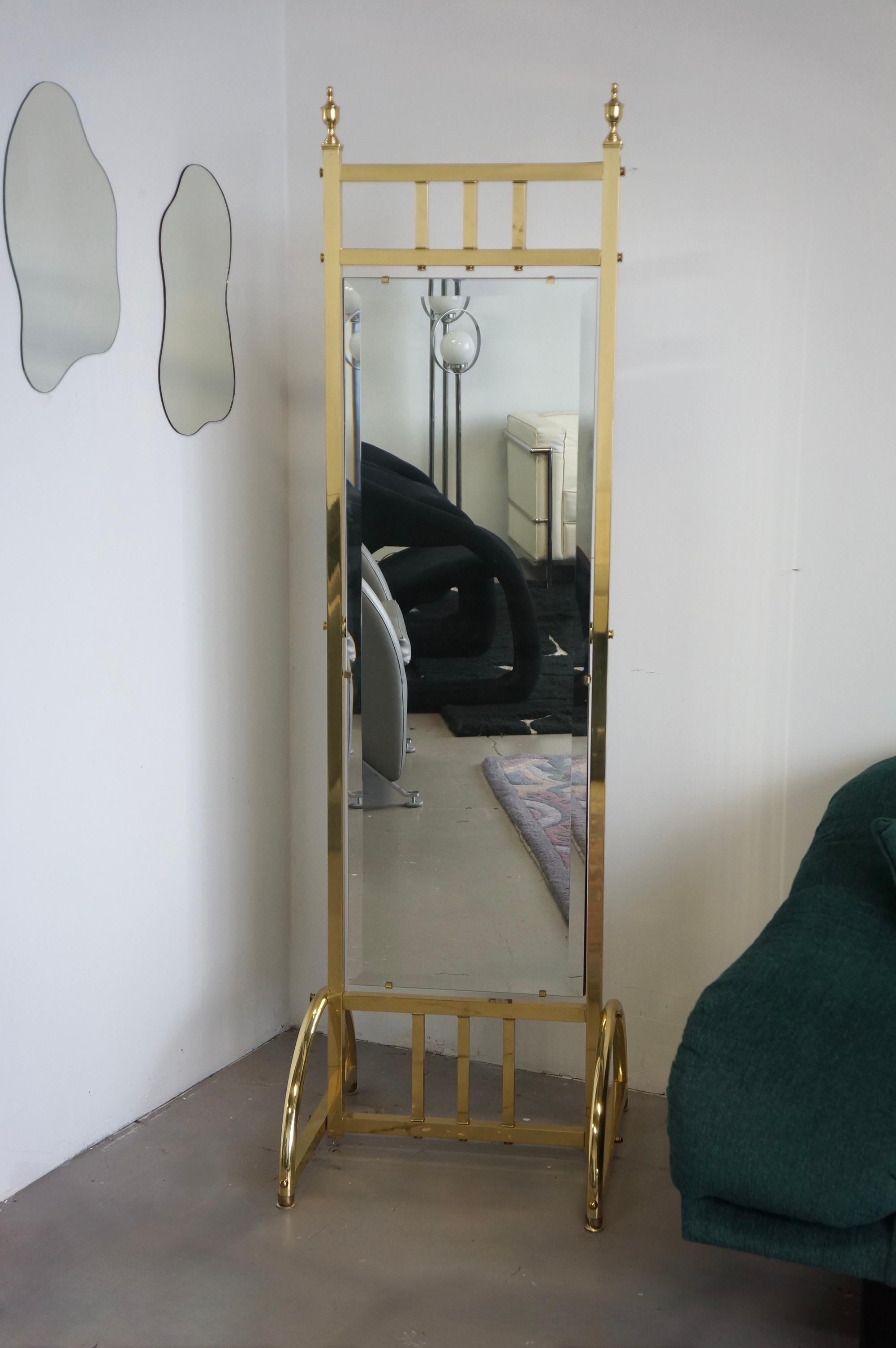 Gorgeous Hollywood regency style brass standing mirror. This mirror has a brass body with a beveled mirror that is held with a wooden backing. There are beautiful detailing throughout such as the crowns on the top corners. The mirror tilts which can