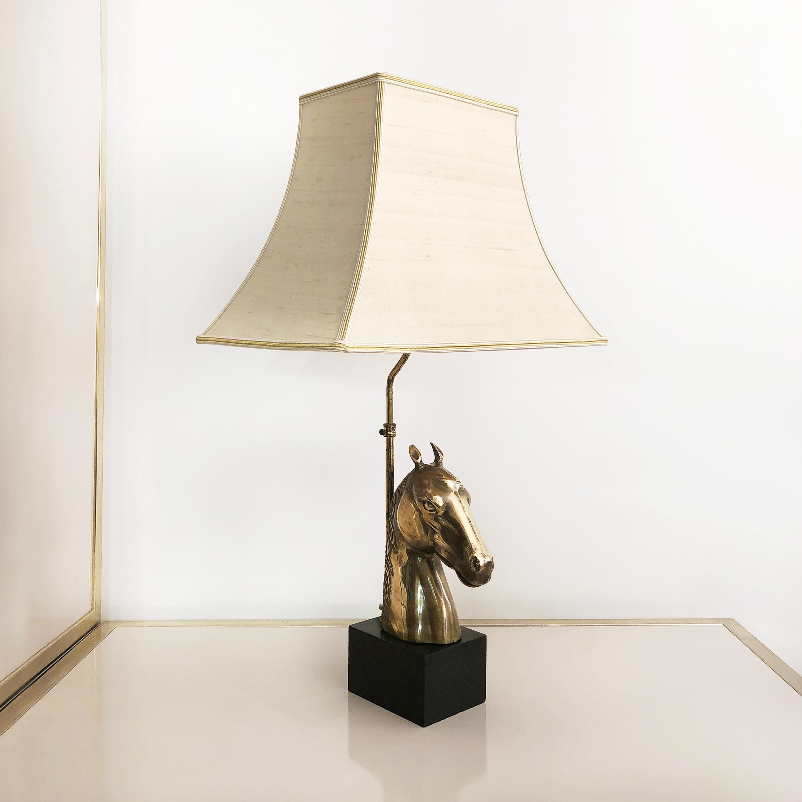An impressive lamp in the shape of brass horse head is supported by a refinished black wooden cube, with chinoiserie shade. The cream square out scallop bell lampshade is very much in keeping with the grandeur of 1970s design.

It is currently