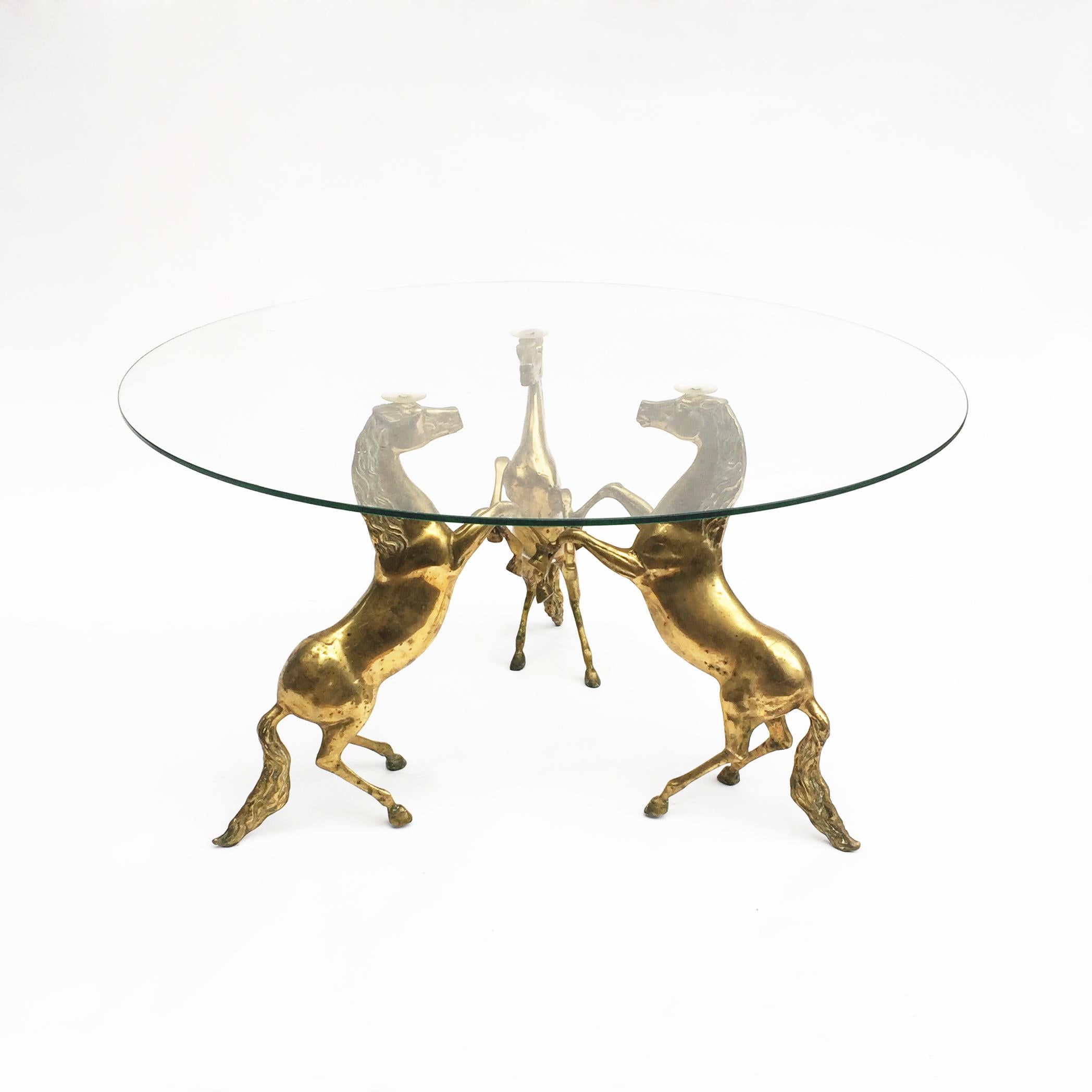 A unique three rearing brass horses table base with its original patina, supporting a round glass top. It can be used as a coffee table or side table. A true Hollywood Regency item.

Base can be shipped outside Europe if requested without the