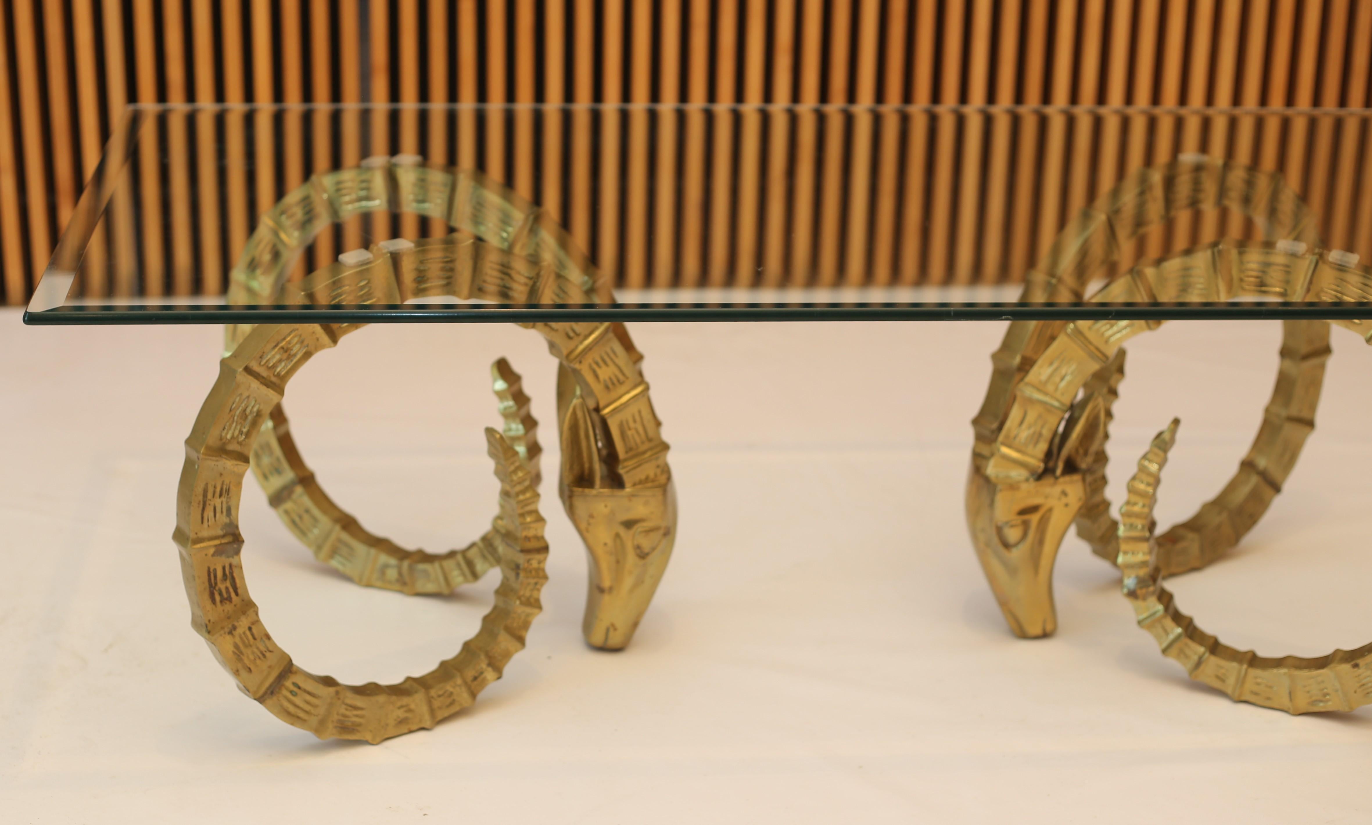 A striking Mid-Century Modern solid brass ibex or ram's head coffee table with glass top from the 1970s. The rectangular glass top shows very well and features a bevelled edge. The brass shows great patina with some Verdigris spots and darker spots.