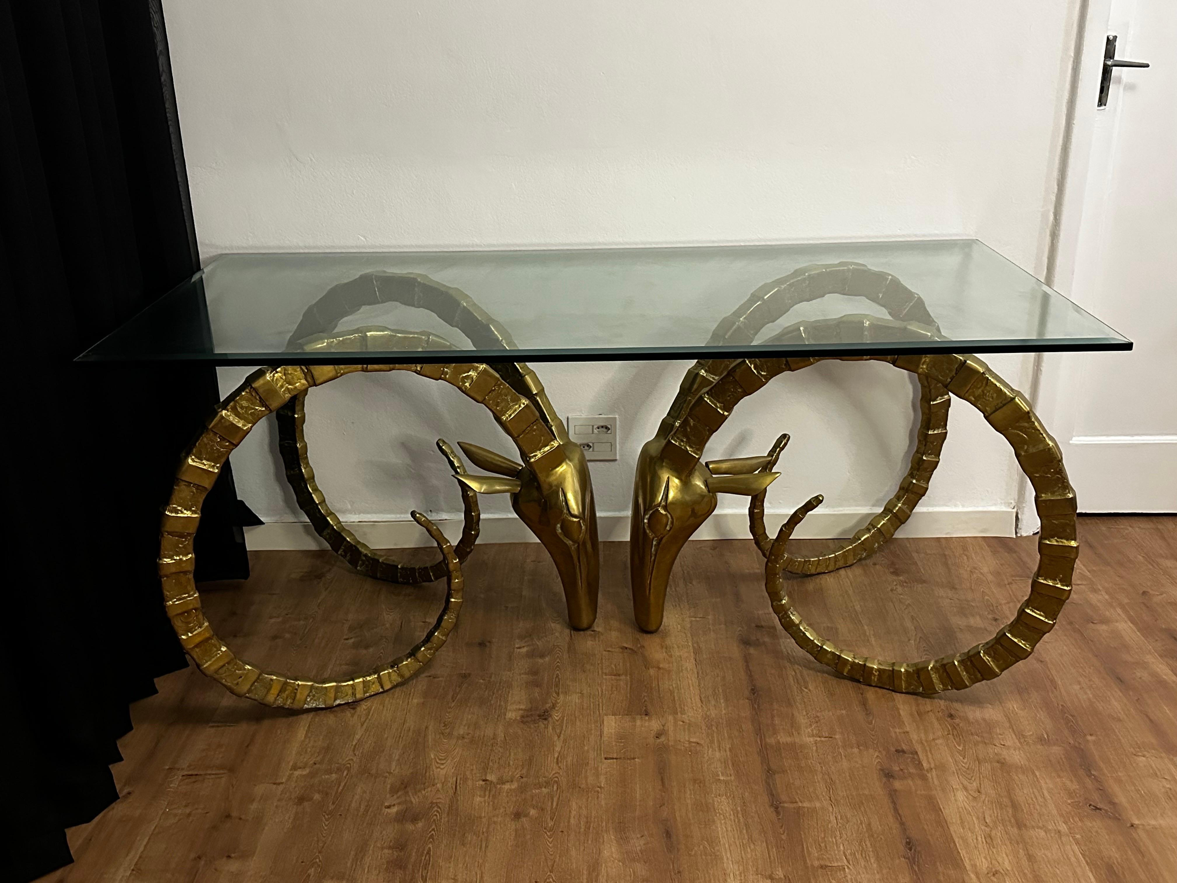 Alain Chervet mid-century modern style glass dining or center table with a pair of brass rams head bases.