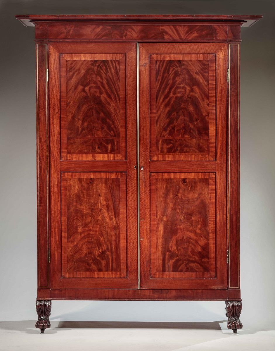 New York, circa 1820.

The flat projecting cornice over a knife-edge molding above a case with pilasters with brass string inlay flanking a pair of highly figured, paneled and cross-banded cabinet doors with brass hinges and astragal, opening to a