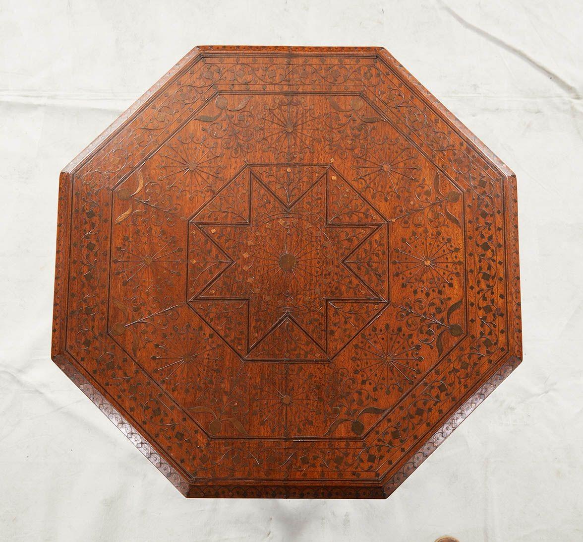 A table with octagonal top over an octagonal base with arched apron and lower surrounding stretcher, having elaborate, profuse and sophisticated brass inlay decoration including central eight point star and surrounding multipoint geometric flowers