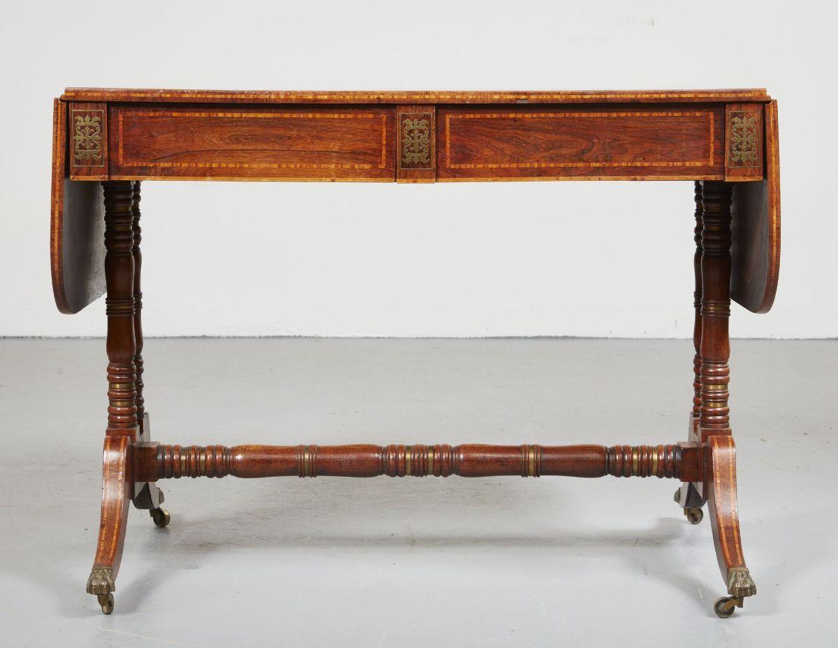 Very fine English Regency rosewood sofa table circa 1820 with satinwood crossbanding and brass inlay, the perfectly sunfaded top with shaped drop flaps, all with double bands of satinwood inlay, over two drawers similarly banded and with brass