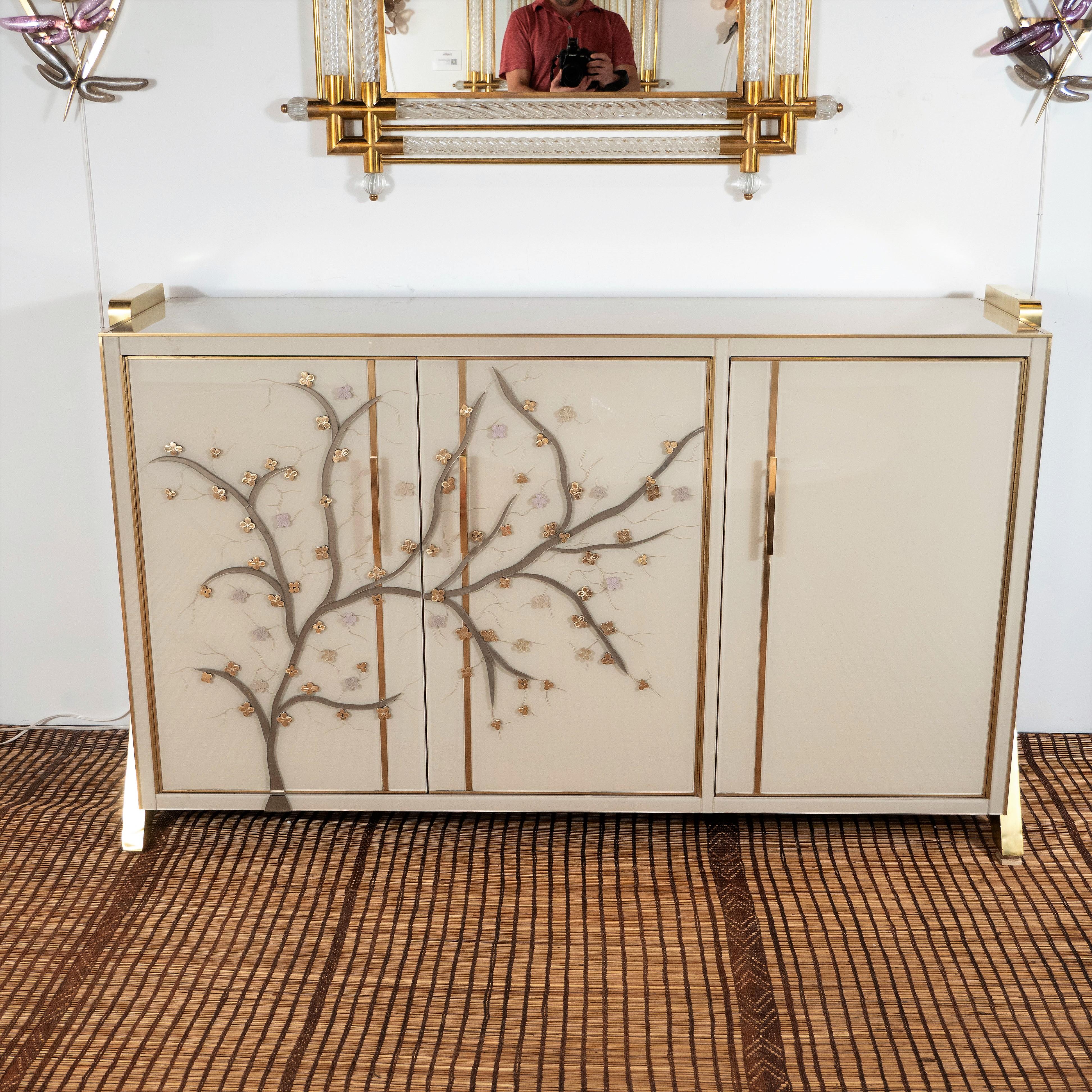 One of a kind sideboard handmade in Venice, Italy by a master artisan and artist. Wooden frame is covered in ivory hand painted Murano glass panels with brass inlays. Handmade and handcut multicolored glass flowers in pearl, lavender and metallic