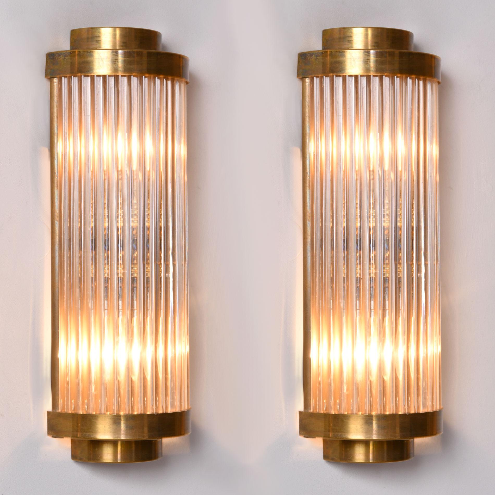 This ‘Ravello’ wall light takes its inspiration from a timelessly classic Art Deco design.
Multiple Italian glass rods form a semi-circle which is capped, top and bottom by 2 tiers of curved brass. The brass back plate holds two light bulbs and