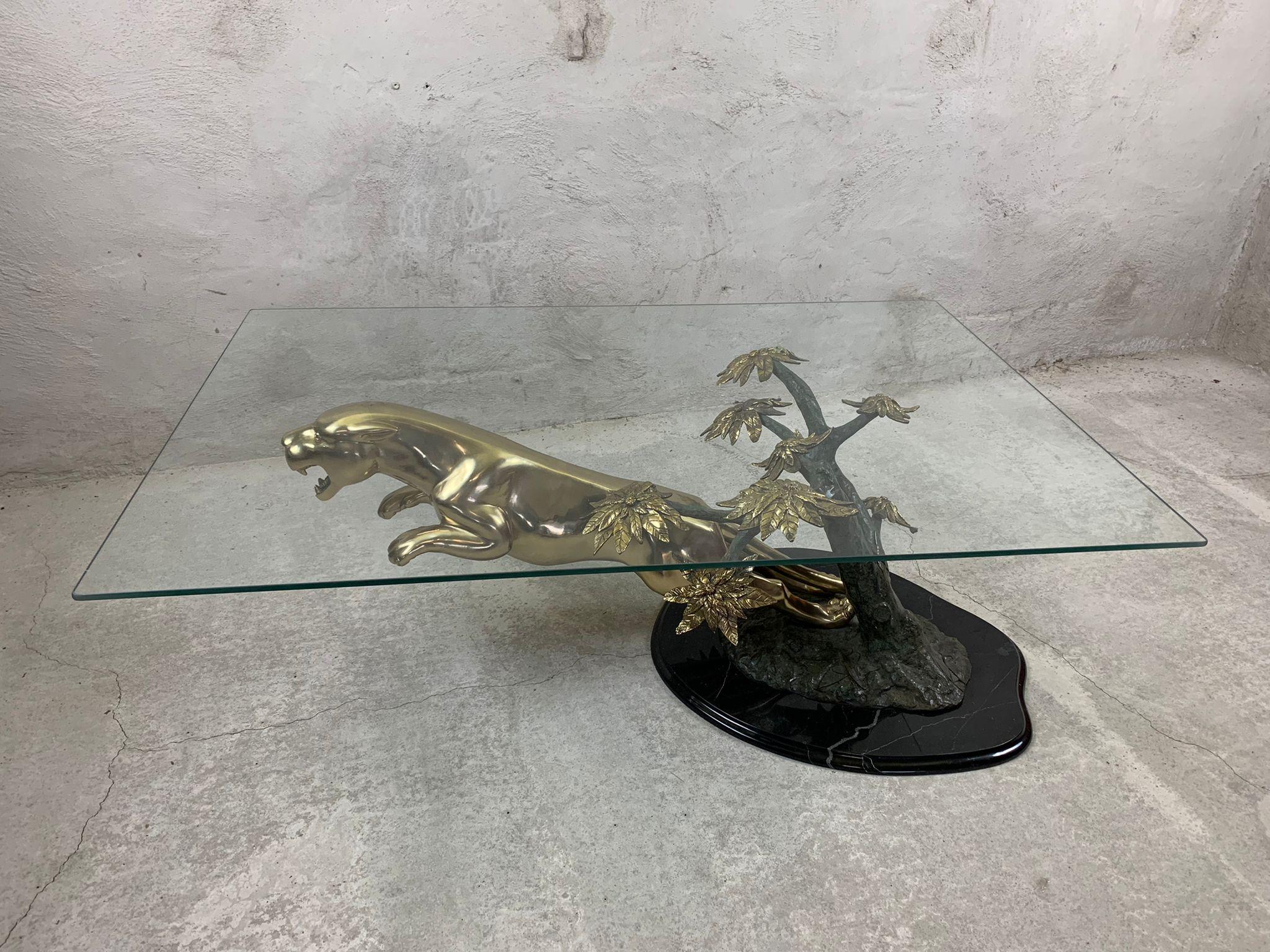 Spectacular coffee table depicting a leaping jaguar which has been sculpted nicely and made from brass.

It is mounted on a black marble base which features a bronze tree with sculpted brass flowers supporting a clear glass top.

1970s - Belgium