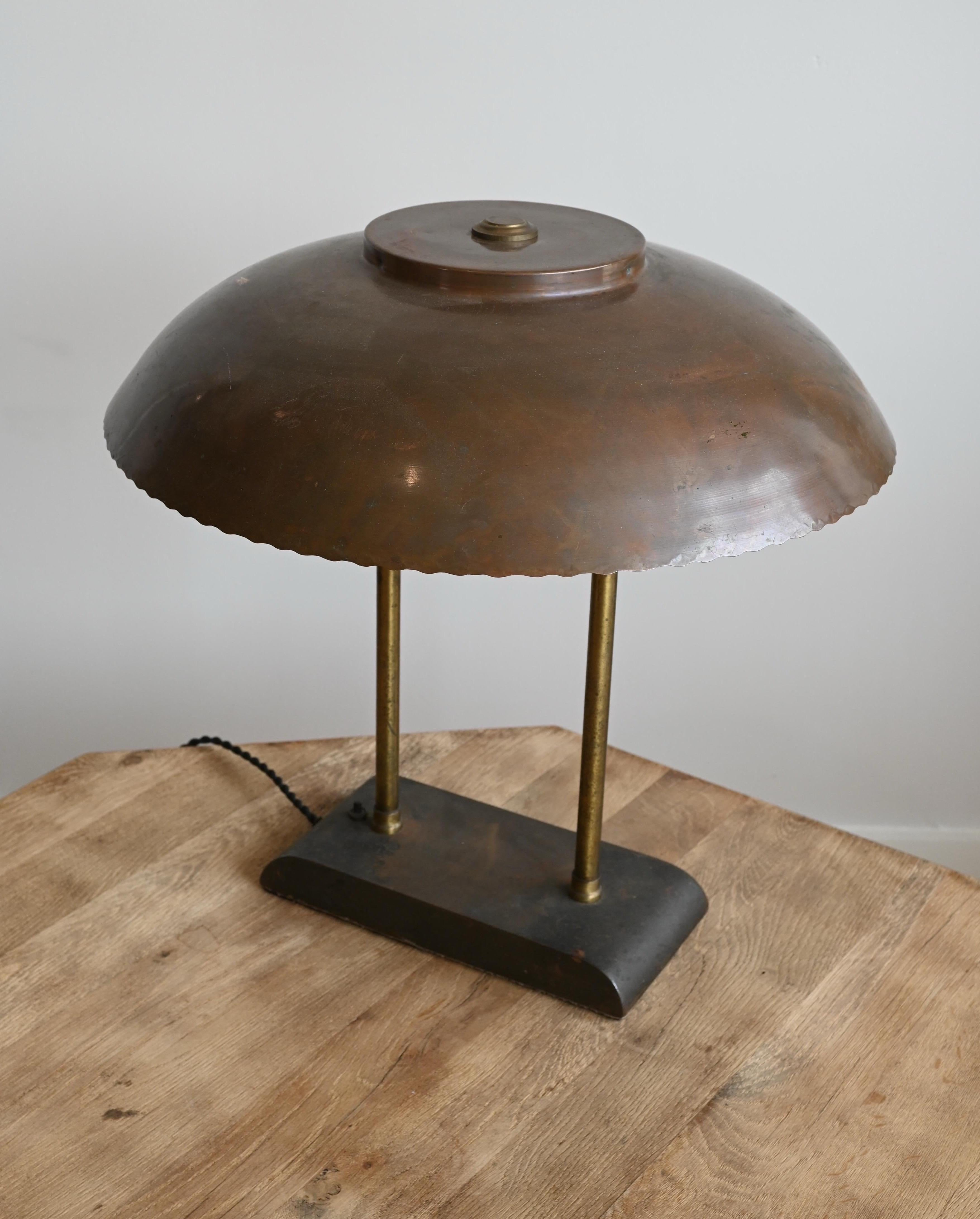 Eine einzigartige Lampe. Einfacher Sockel mit Einschalttaste. Der Leuchtenkörper besteht aus zwei schlichten Messingstäben, die zu einem Kupferschirm mit Wellenschliff führen. 