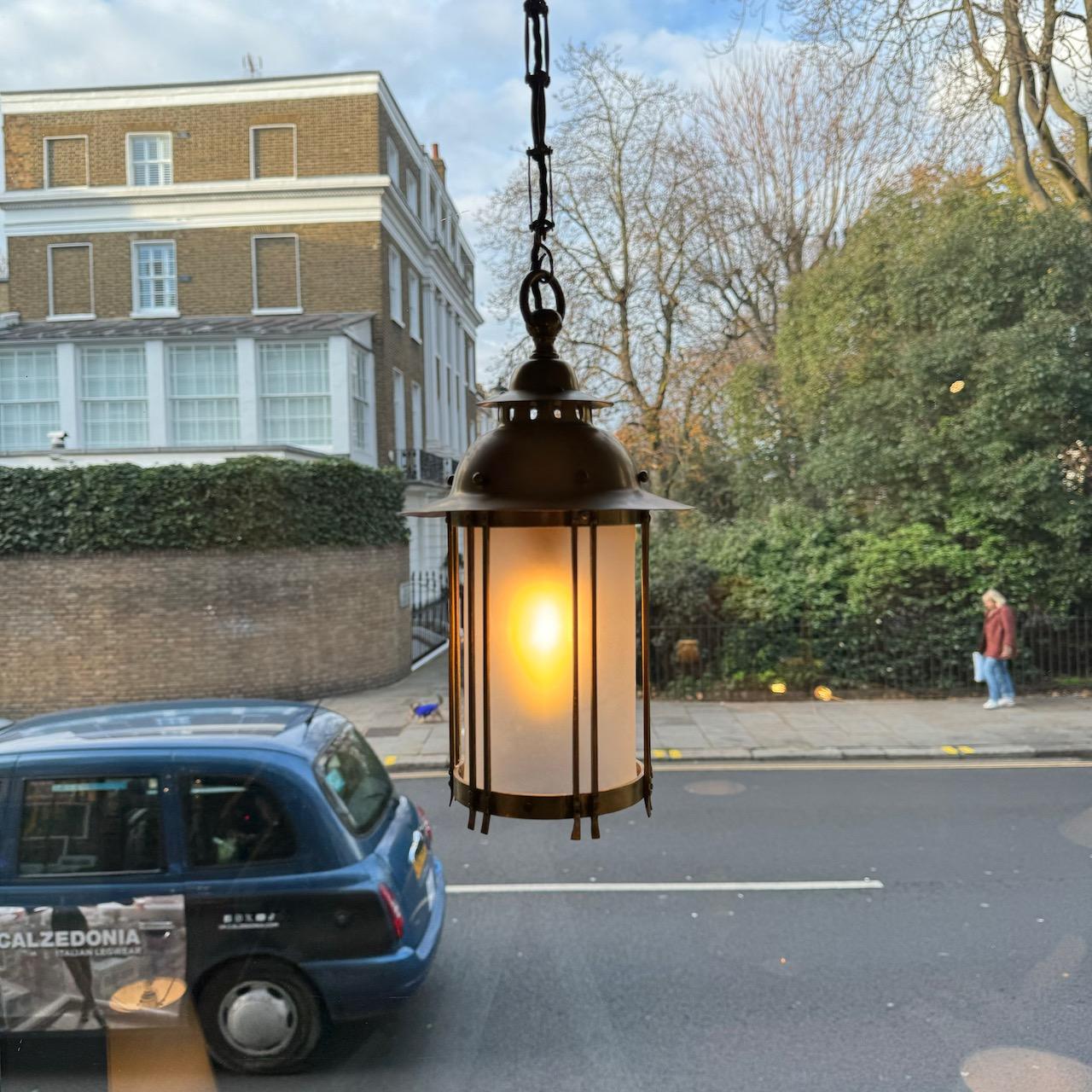 This brass lantern was made in Britain between 1908-1909. 

The lantern is suspended by a chain of rectangular brass links, echoing the linearity of the overall design. The neck of the lantern is articulated with cut-away ovals, whilst spherical