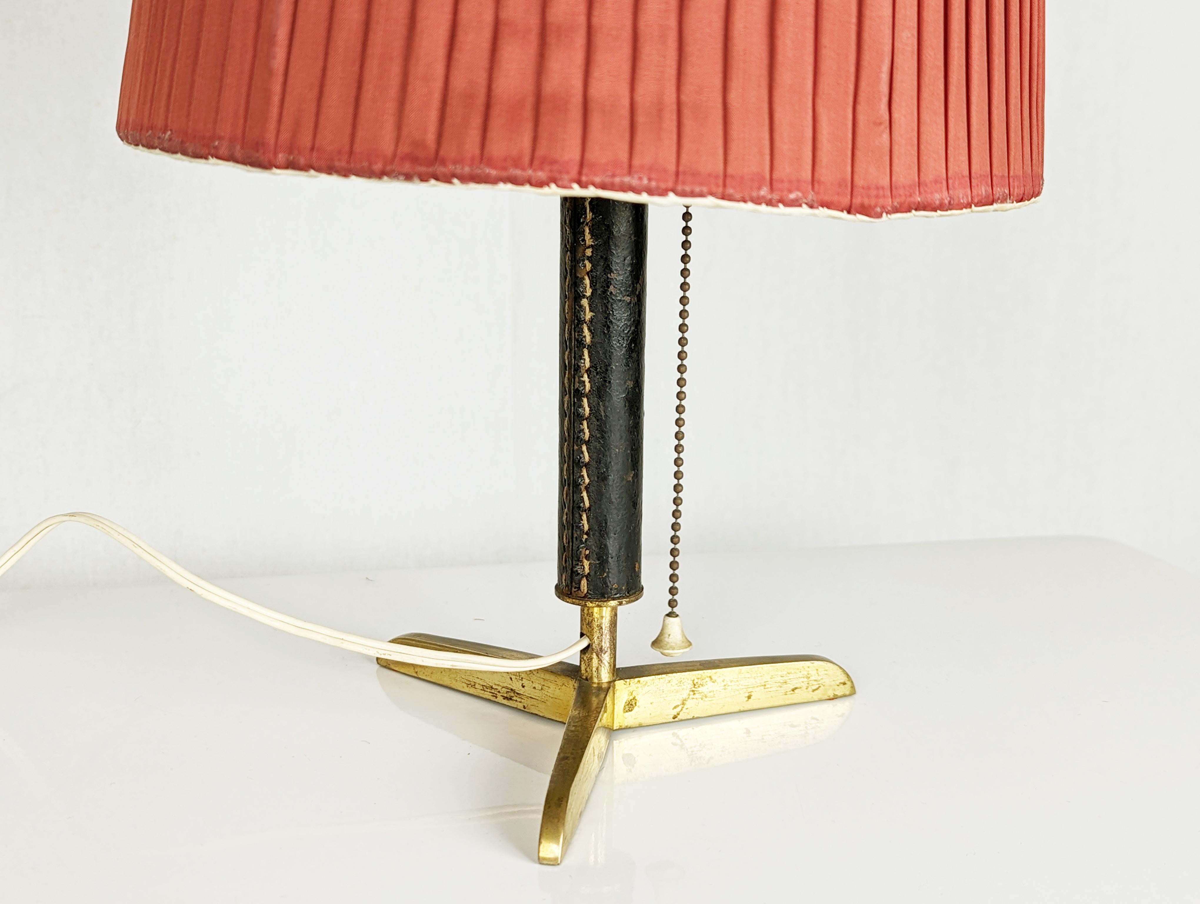 Petite lampe de table/abat jour en structure laiton avec revêtement en cuir marron. Interrupteur à chaîne incorporé dans la douille de la lampe. Assez bon état : patine d'oxydation et défauts du cuir.

dimensions : cm 27h x 16 p (sans abat-jour en