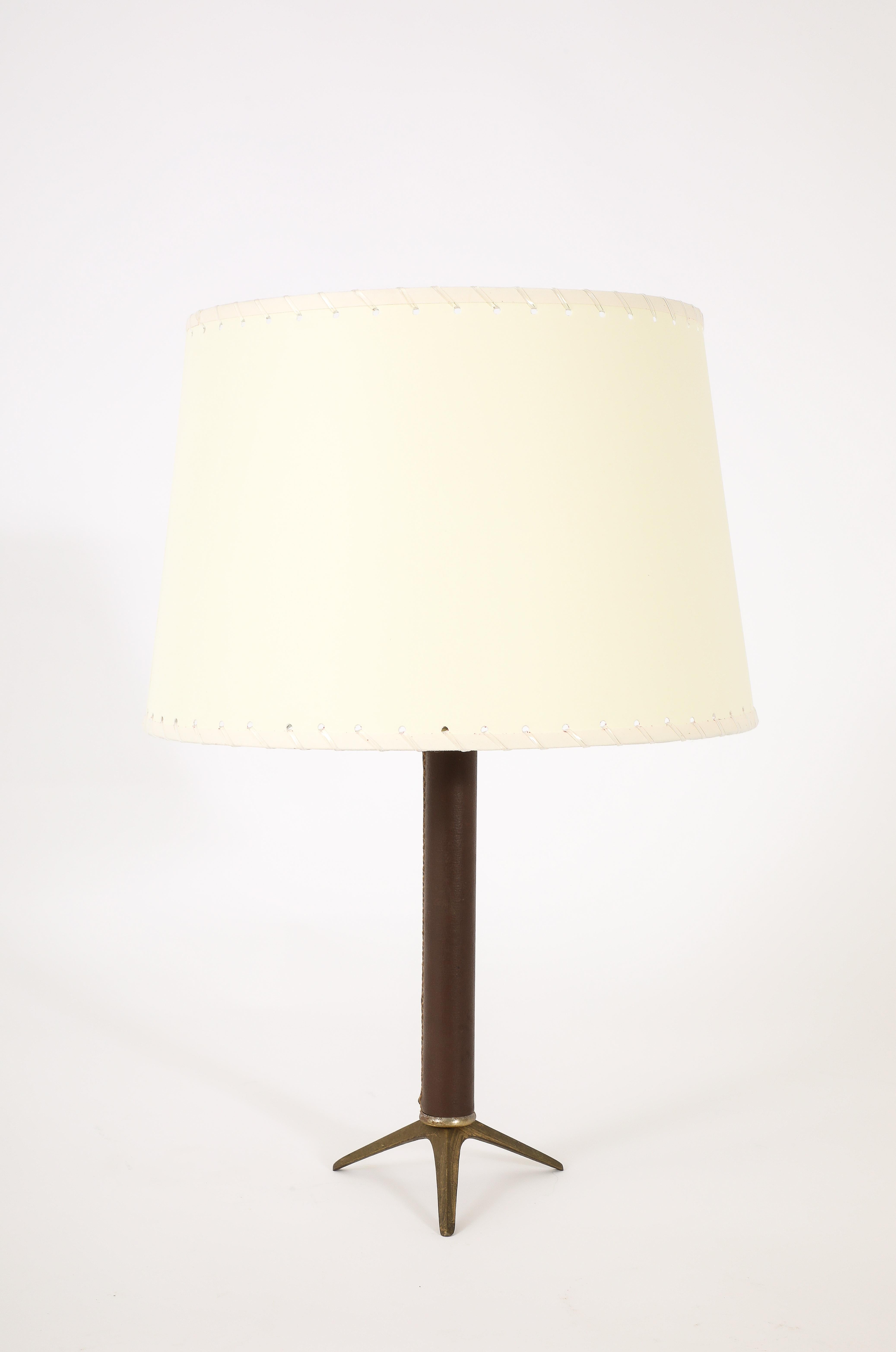 Tischlampe aus dunkelbraunem Leder auf einem Dreibeinfuß.
