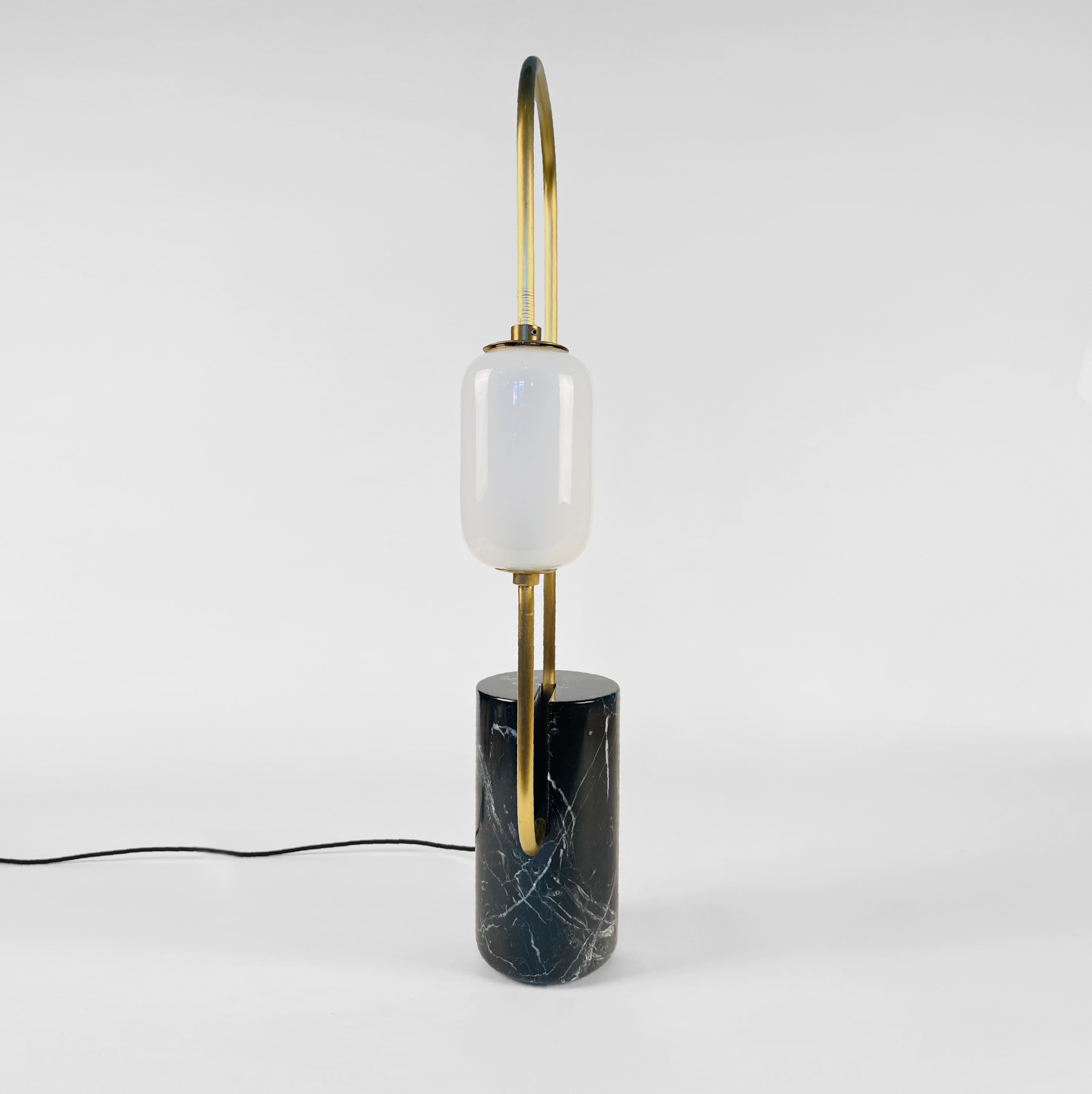 Loop table lamp. Made in black marble and brass lacquered metal pipe that loops around the base and holds a milky white glass capsule shade with a LED lamp.