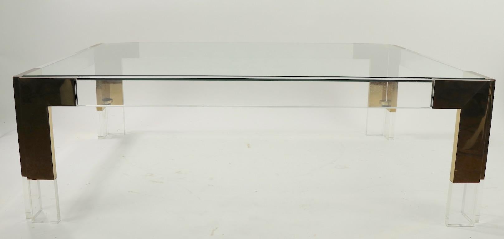 This coffee table has a Lucite frame with brass corner joinery and a plate glass top. It is in very good, original condition, showing only light cosmetic wear, normal and consistent with age. Rectangular form, slick style, design influenced by