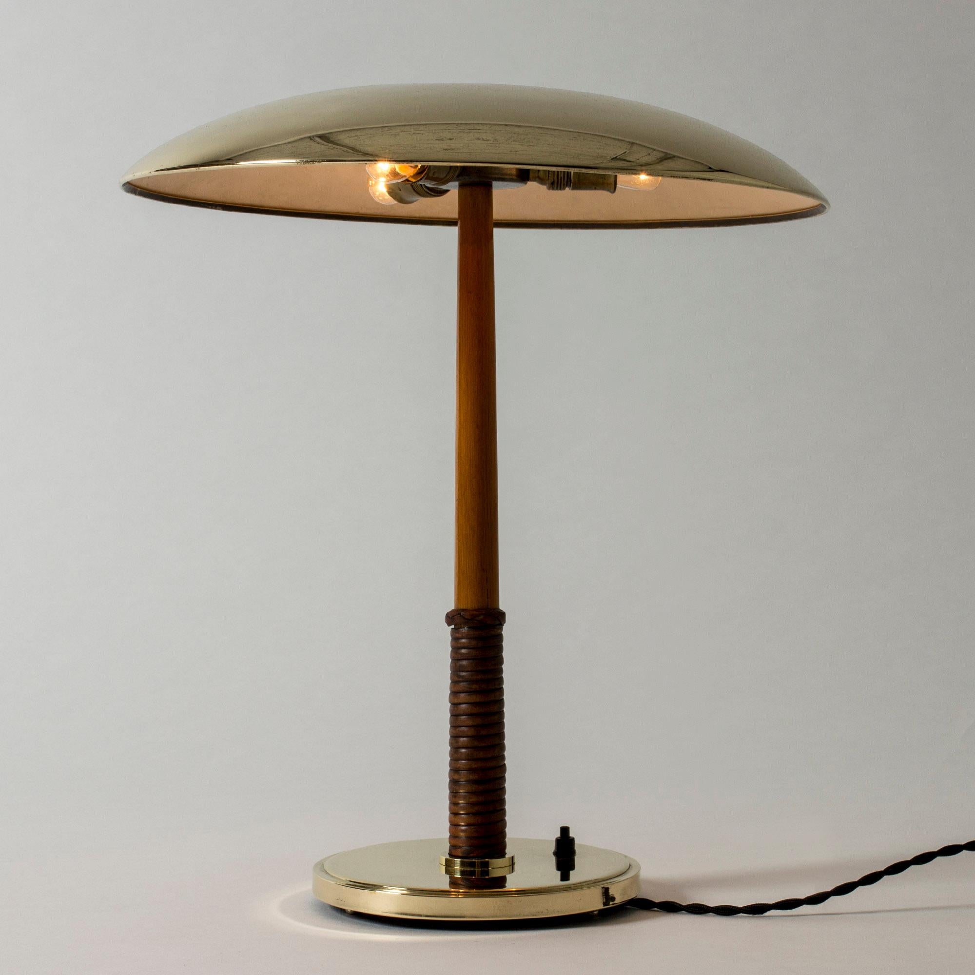 Elegant brass table lamp from Böhlmarks, with a smooth concave disc shade. Mahogany handle wreathed with leather around the base.